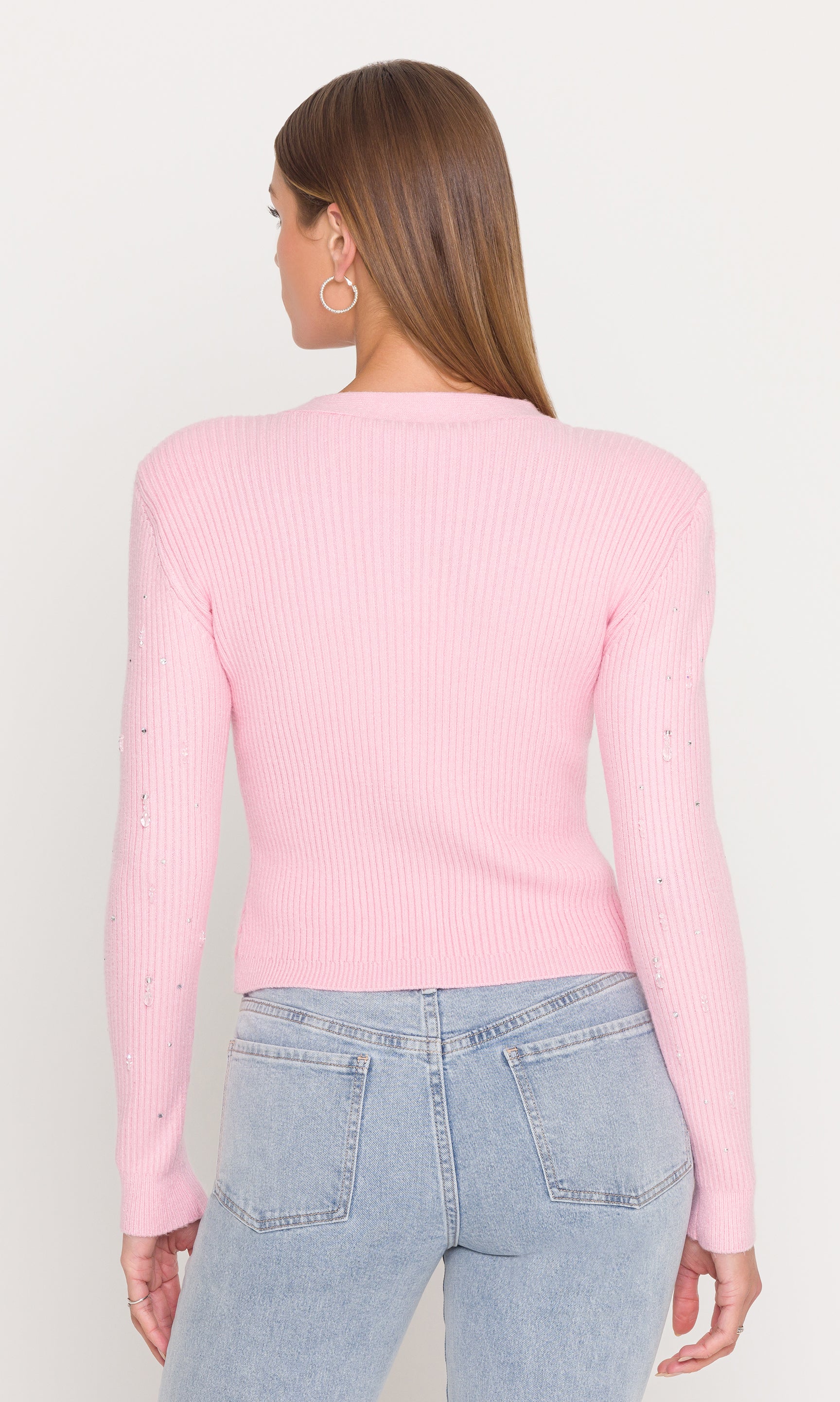 Back view of model wearing a pink ribbed sweater and light blue jeans on a plain background