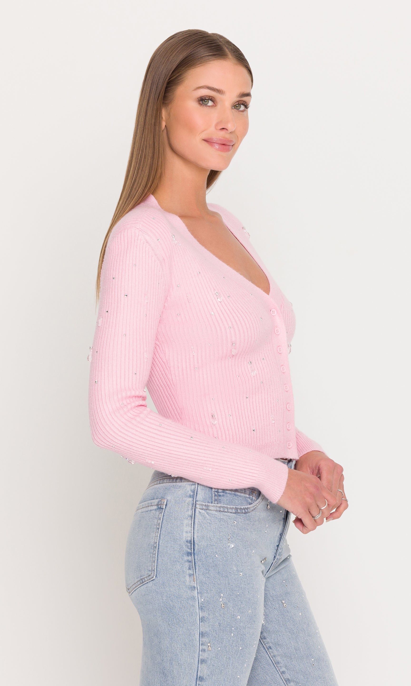 Side view of woman wearing a pink sweater and light blue jeans against a white background