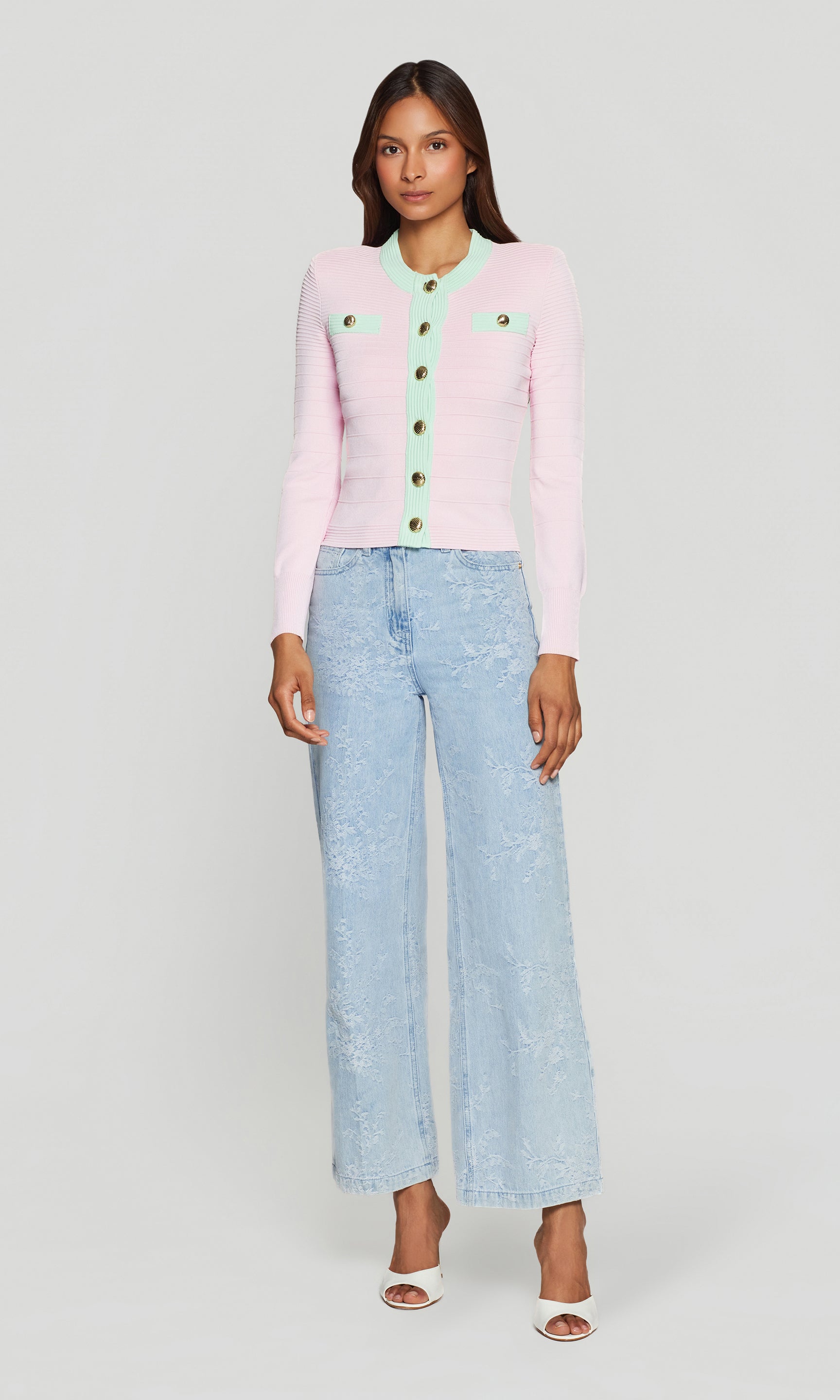 The model appears in a full body front view wearing the Lilla Bandage Cardigan in pink with light wash denim, highlighting the tailored fit and statement buttons.