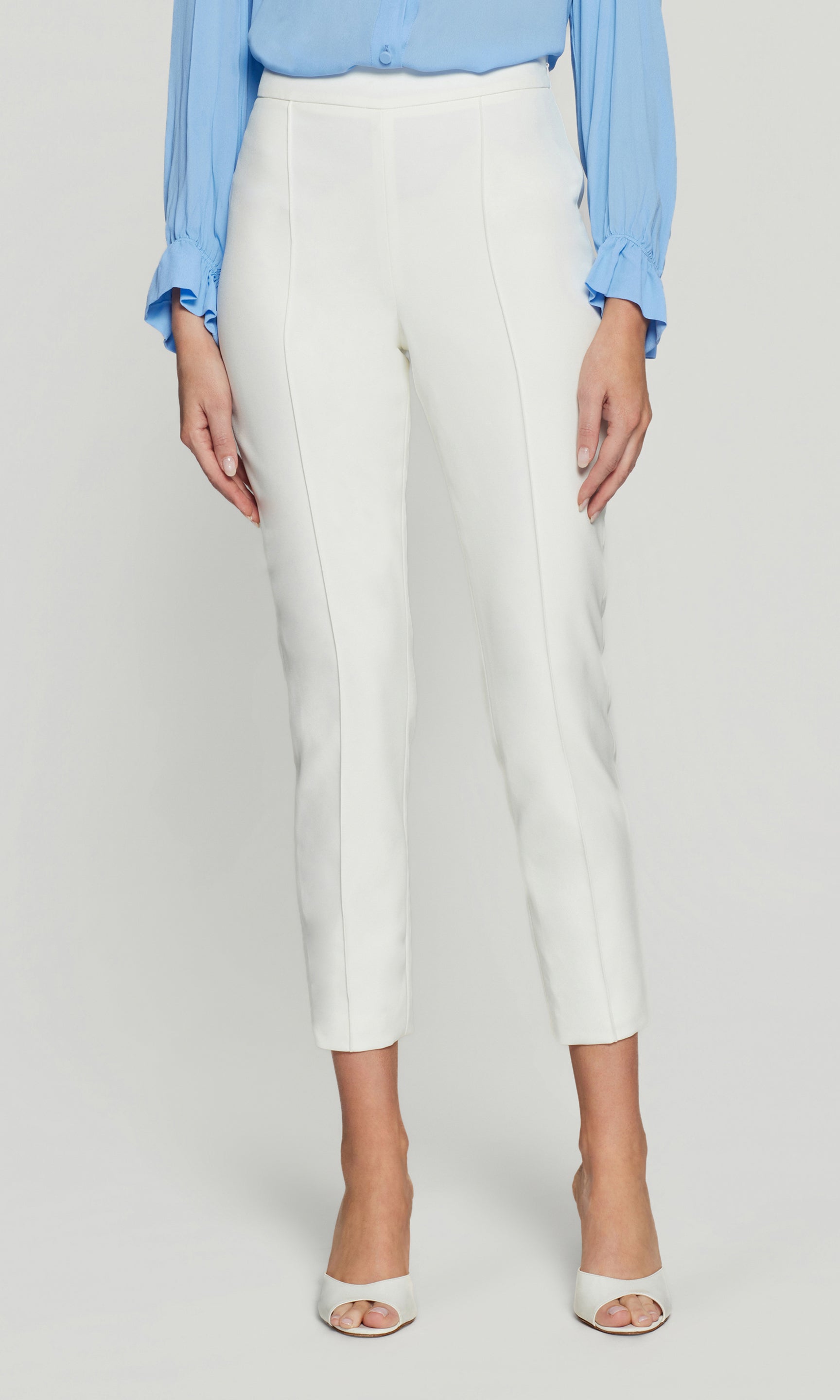 Front view of the model wearing the Lonny Crepe Pants in white, highlighting the high-rise waist, clean front seam, and ankle-length slim leg with heels.