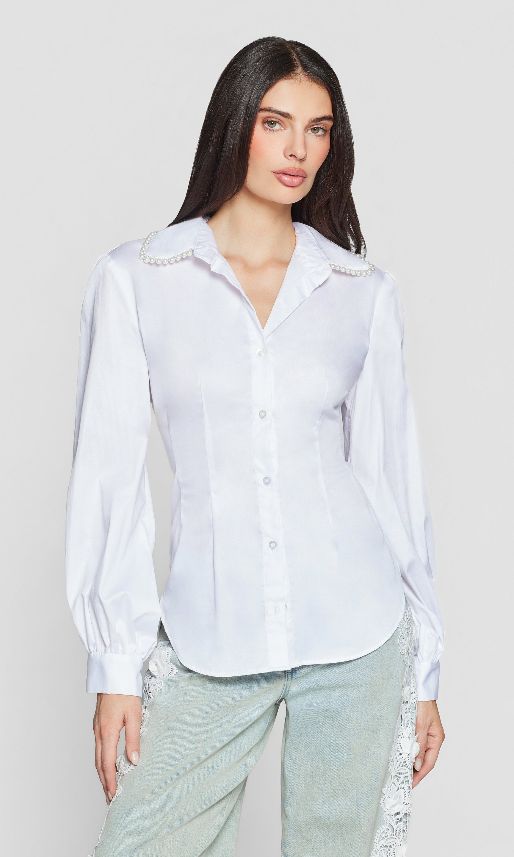 Woman wearing a white blouse with decorative pearl trim on a plain background