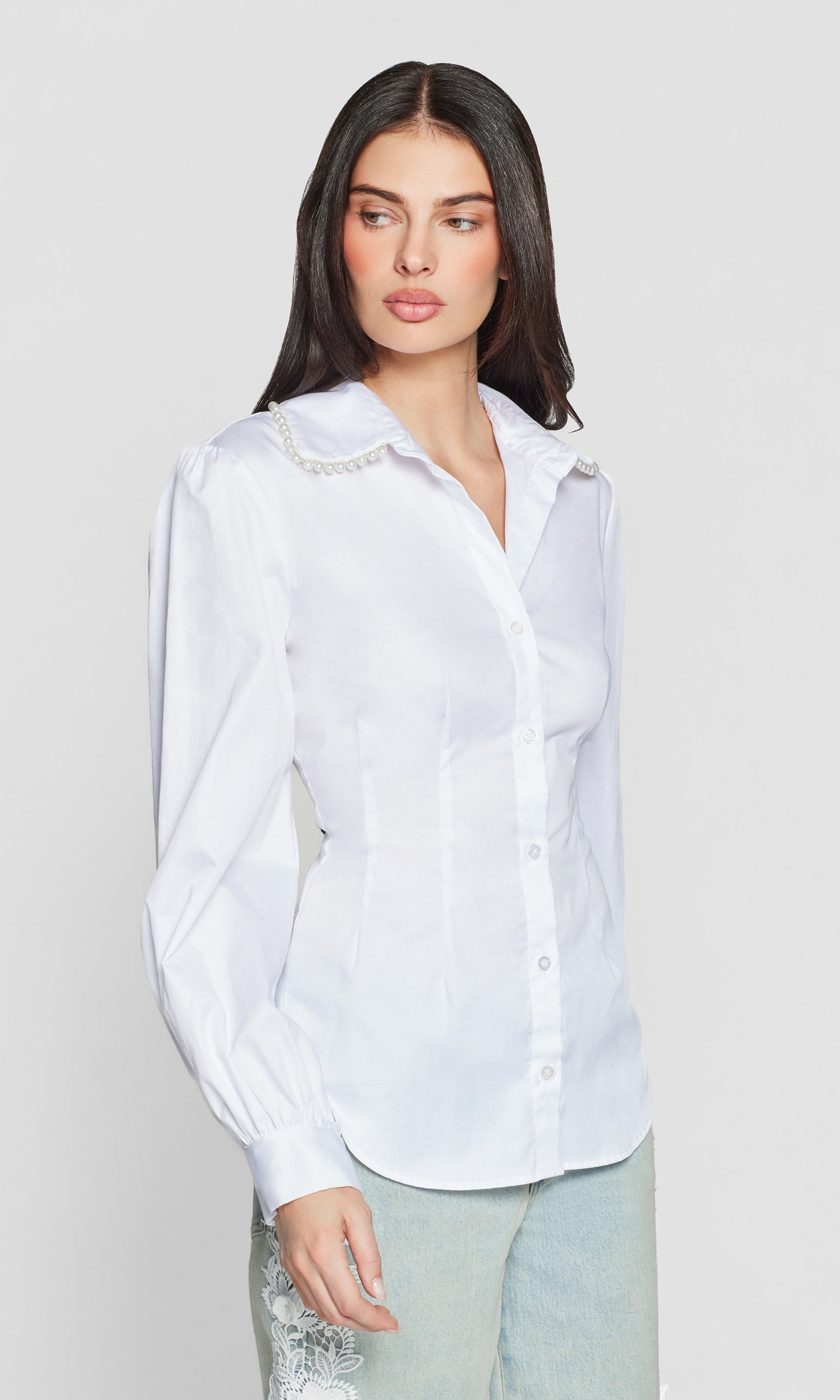Side view of woman wearing a white blouse with decorative pearl trim on a plain background