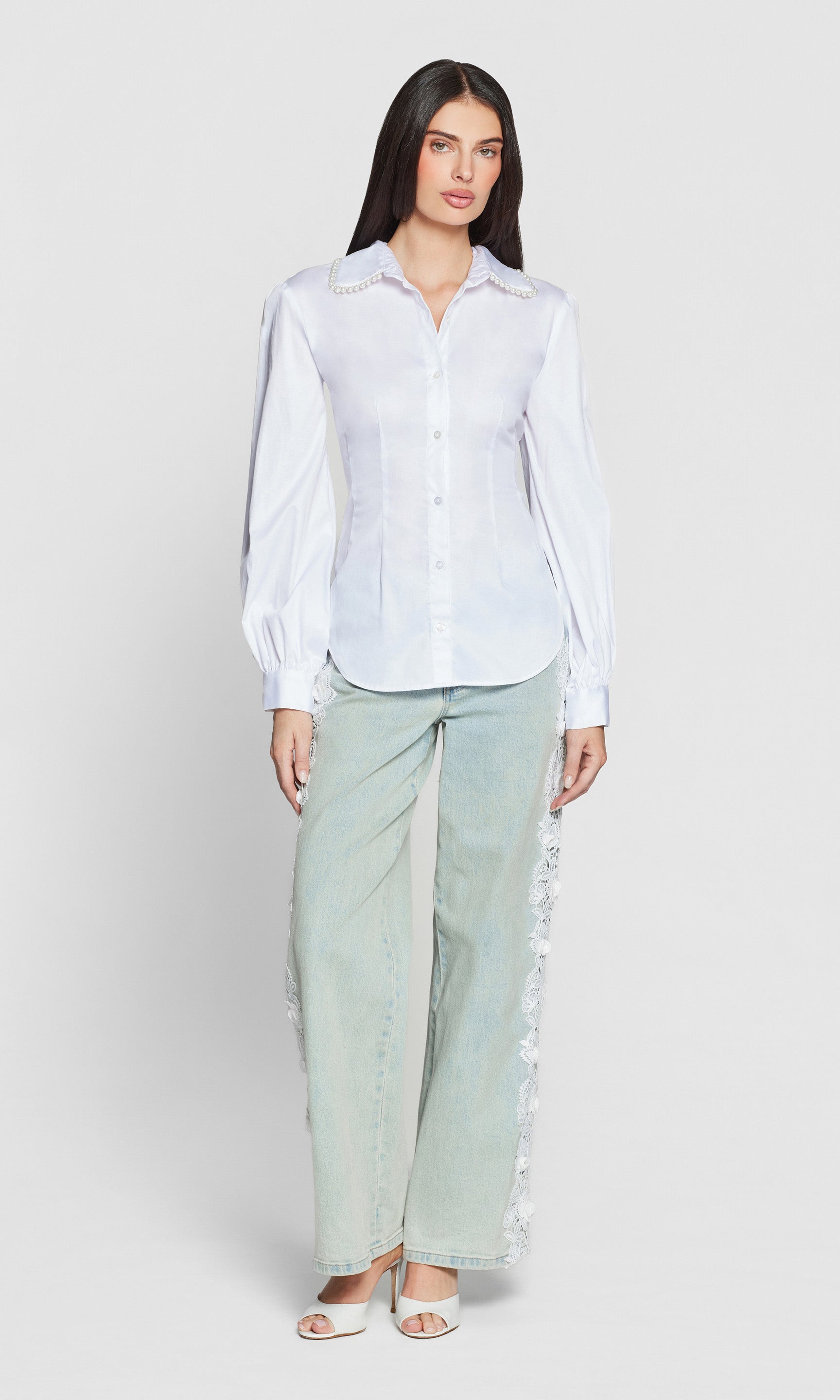 Woman wearing a white pearl embellished top with blue jeans on plain background