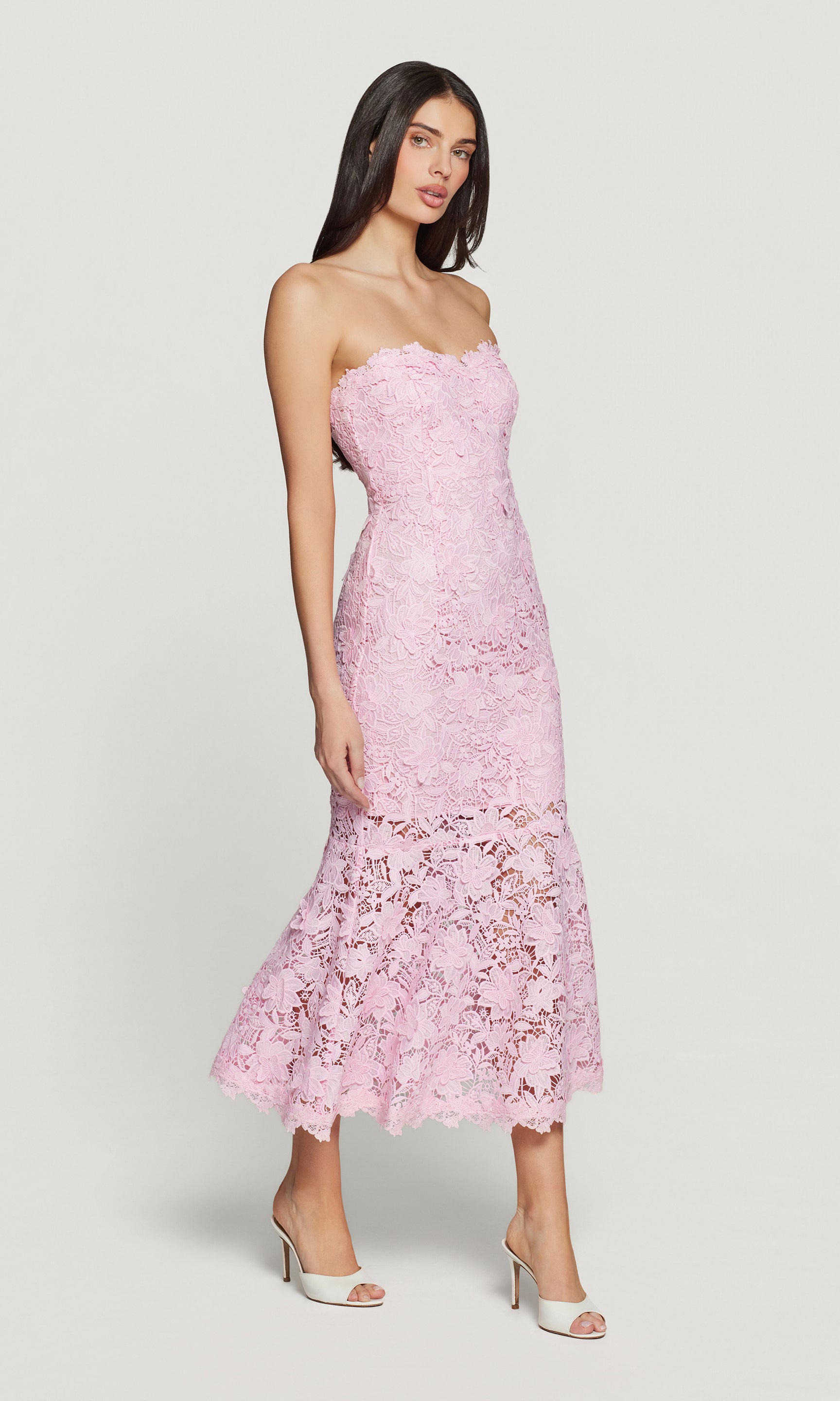 Side view of woman wearing a pink strapless lace dress on a white background