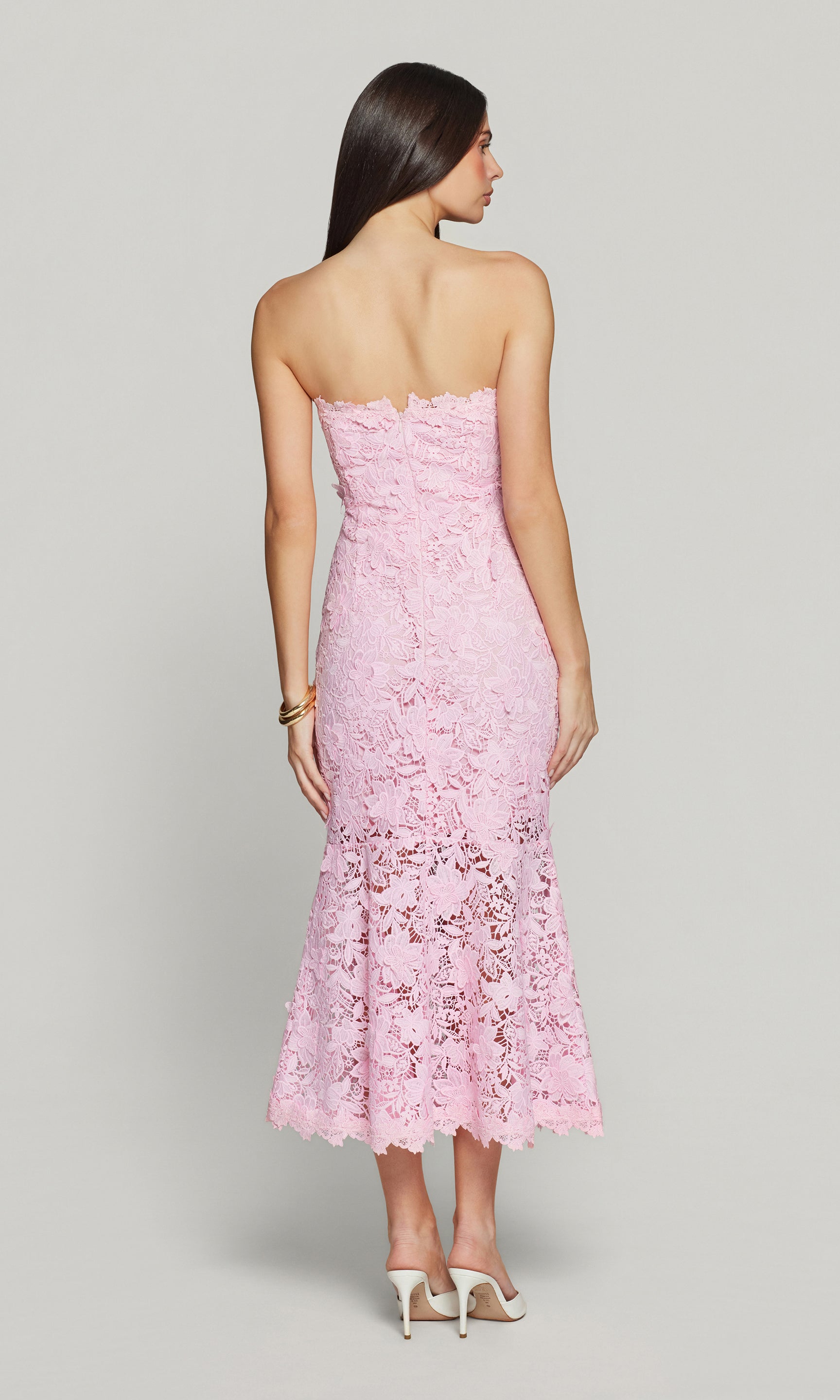 Back view of woman wearing a pink strapless lace dress on a gray background