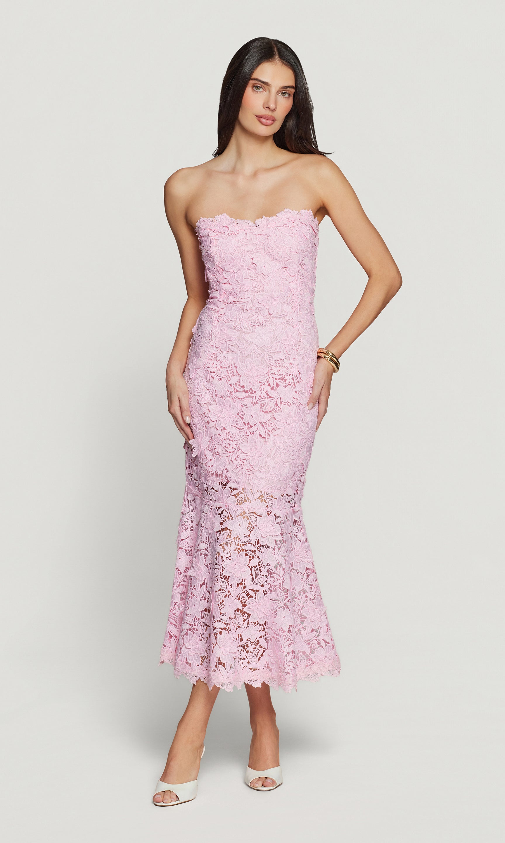 Woman wearing a pink lace strapless dress with white heels on a white background