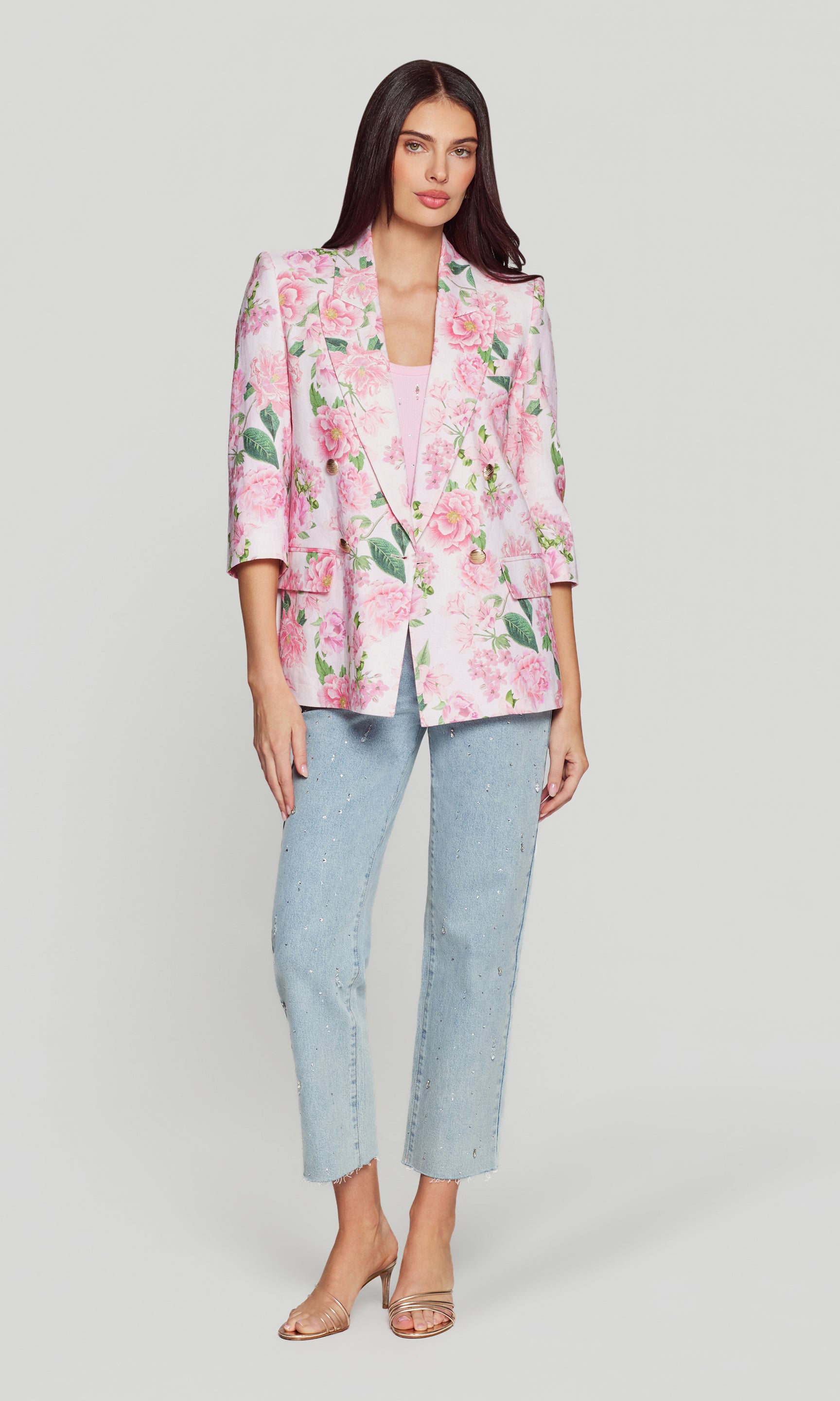 Woman wearing a pink floral blazer, pink tank and light blue jeans on a white background