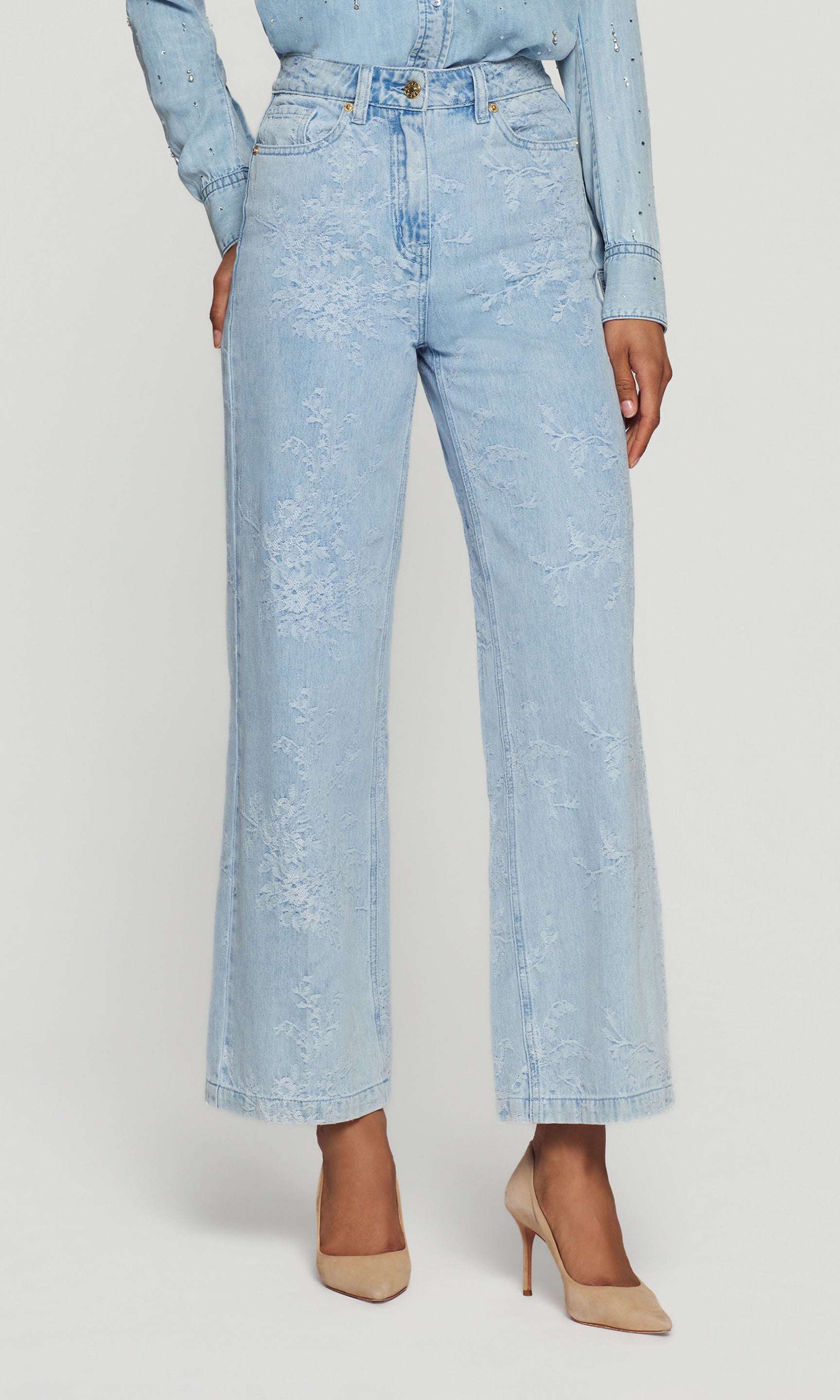 Light blue denim jeans with floral pattern worn by a person on a white background