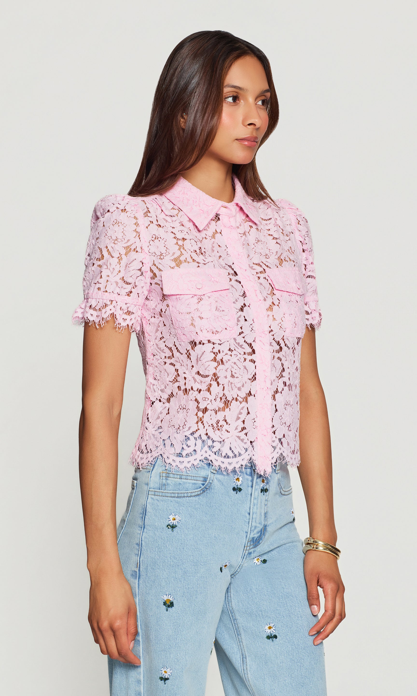 Side view of woman wearing a pink lace blouse and light blue jeans on a white background