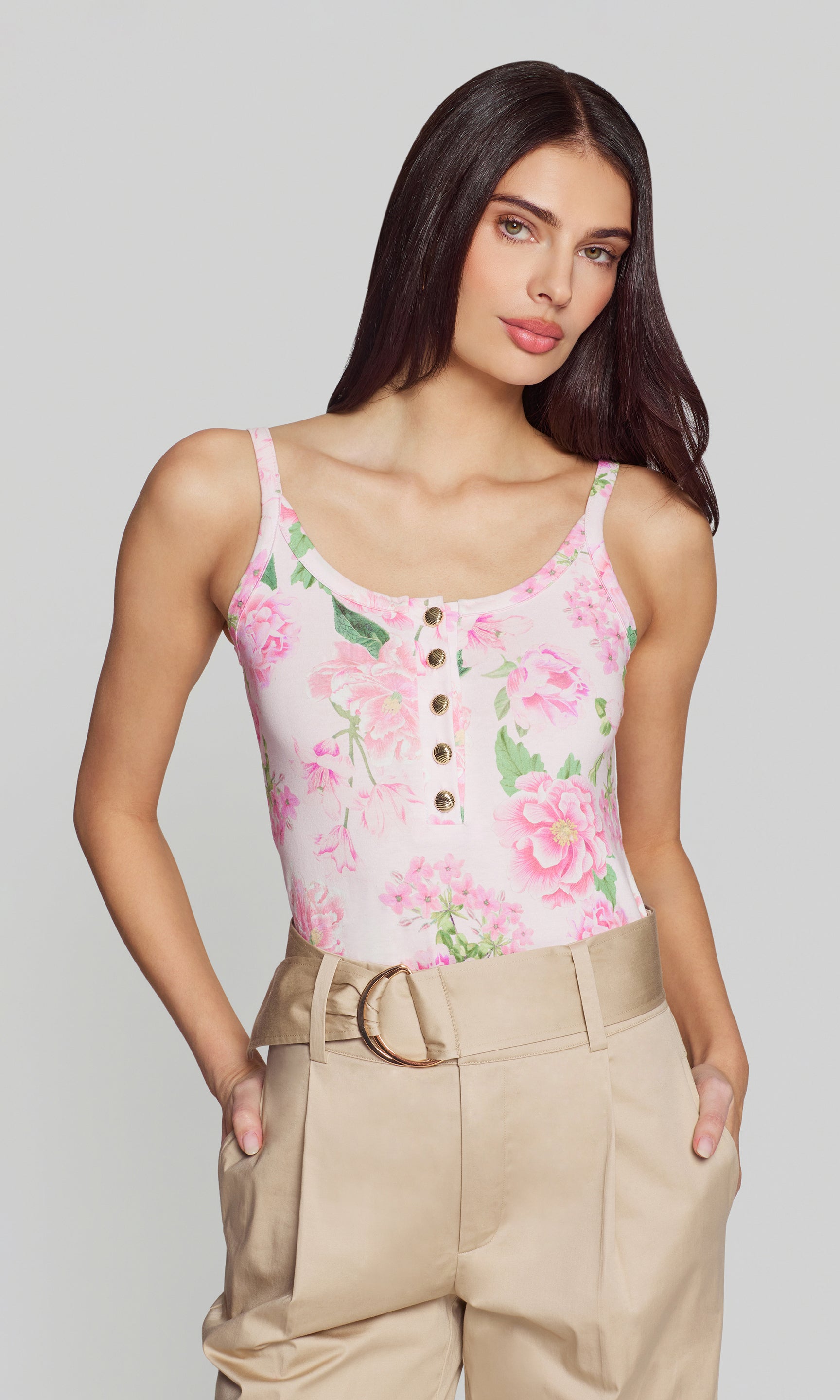 Woman wearing a floral tank top and beige pants on a plain background