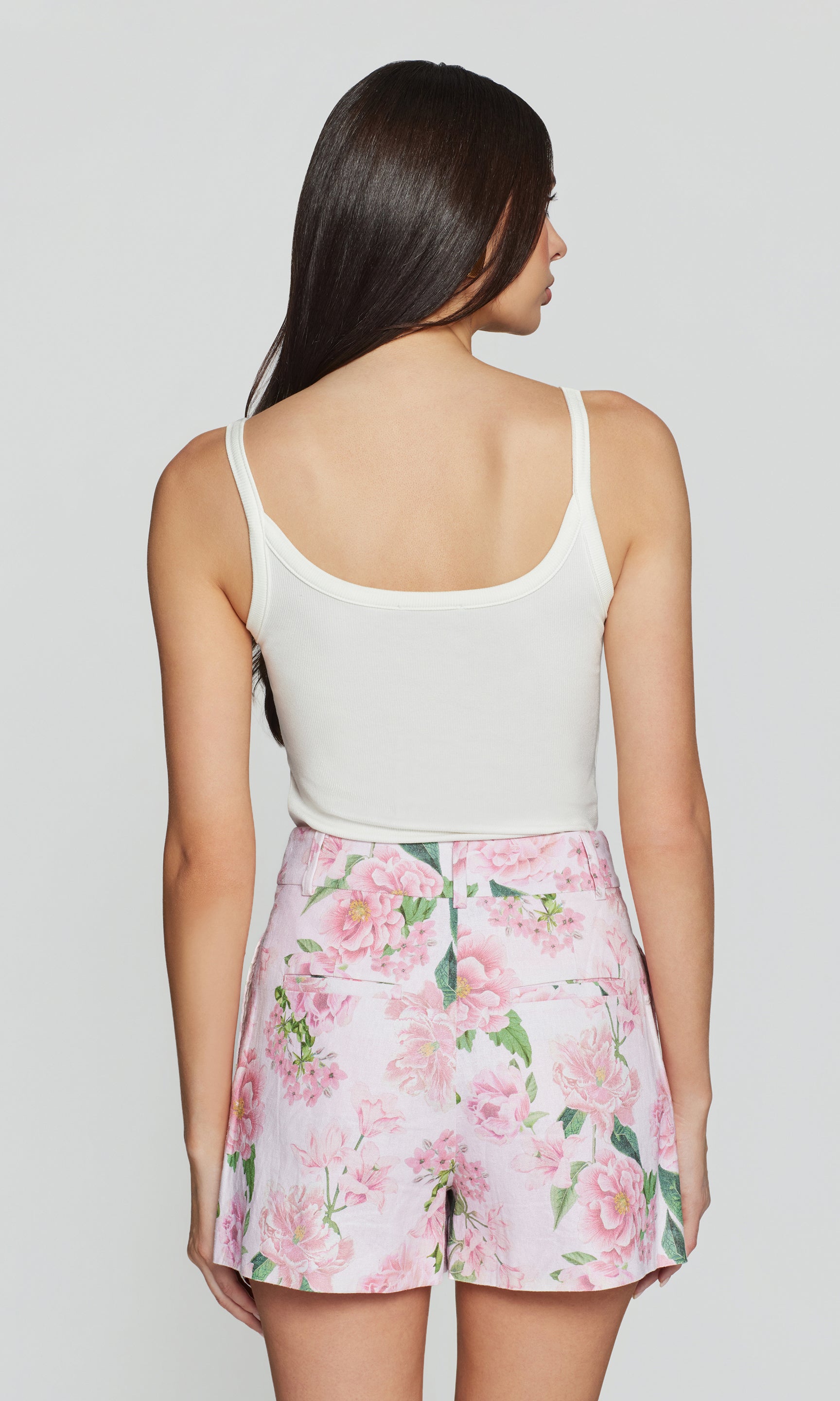 In a rear view, the model wears the Molly Rib Tank Top in white with a floral mini skirt, showing the clean back and slim, body-skimming fit.