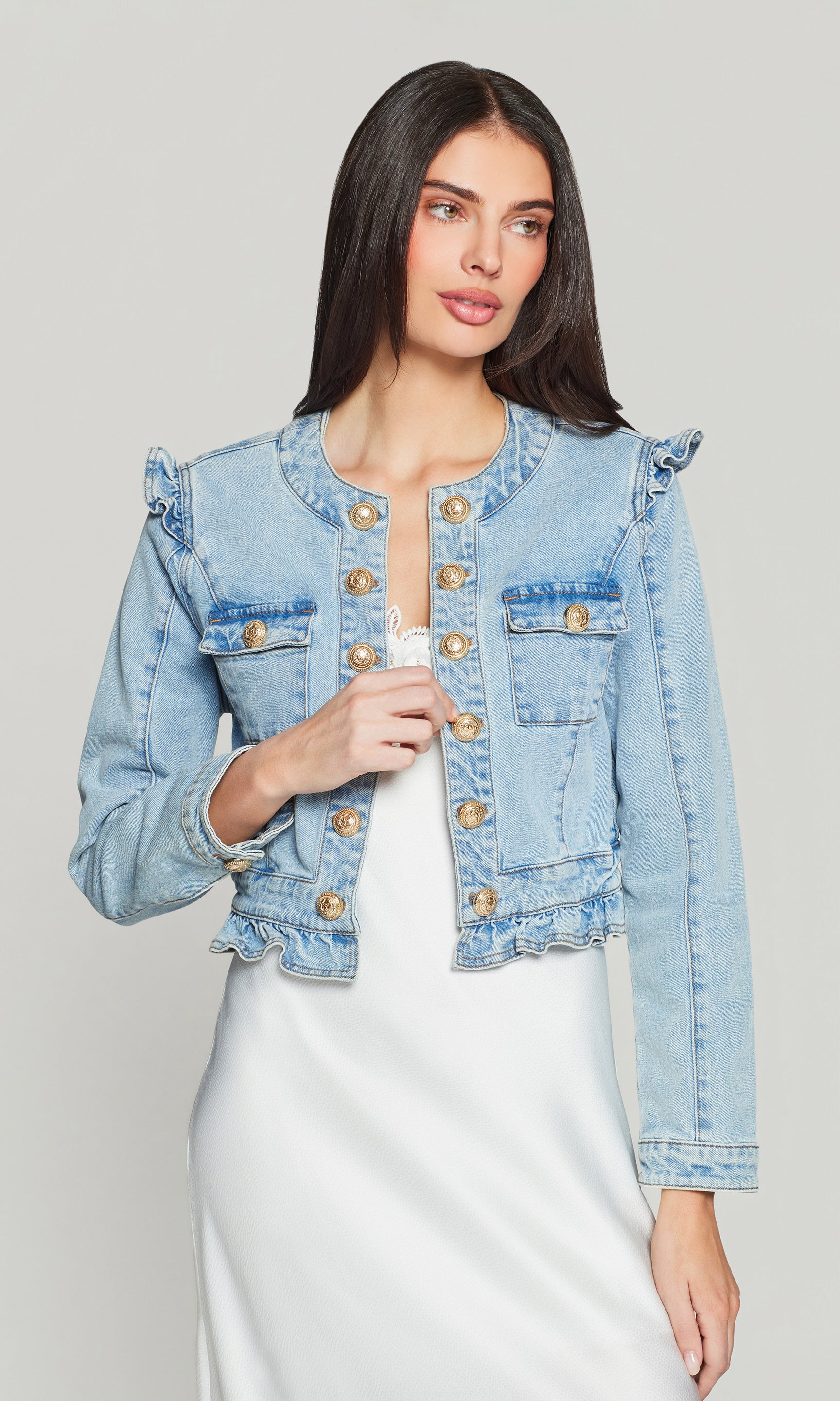 Woman wearing a light blue denim jacket with ruffled shoulder sleeves on a plain background