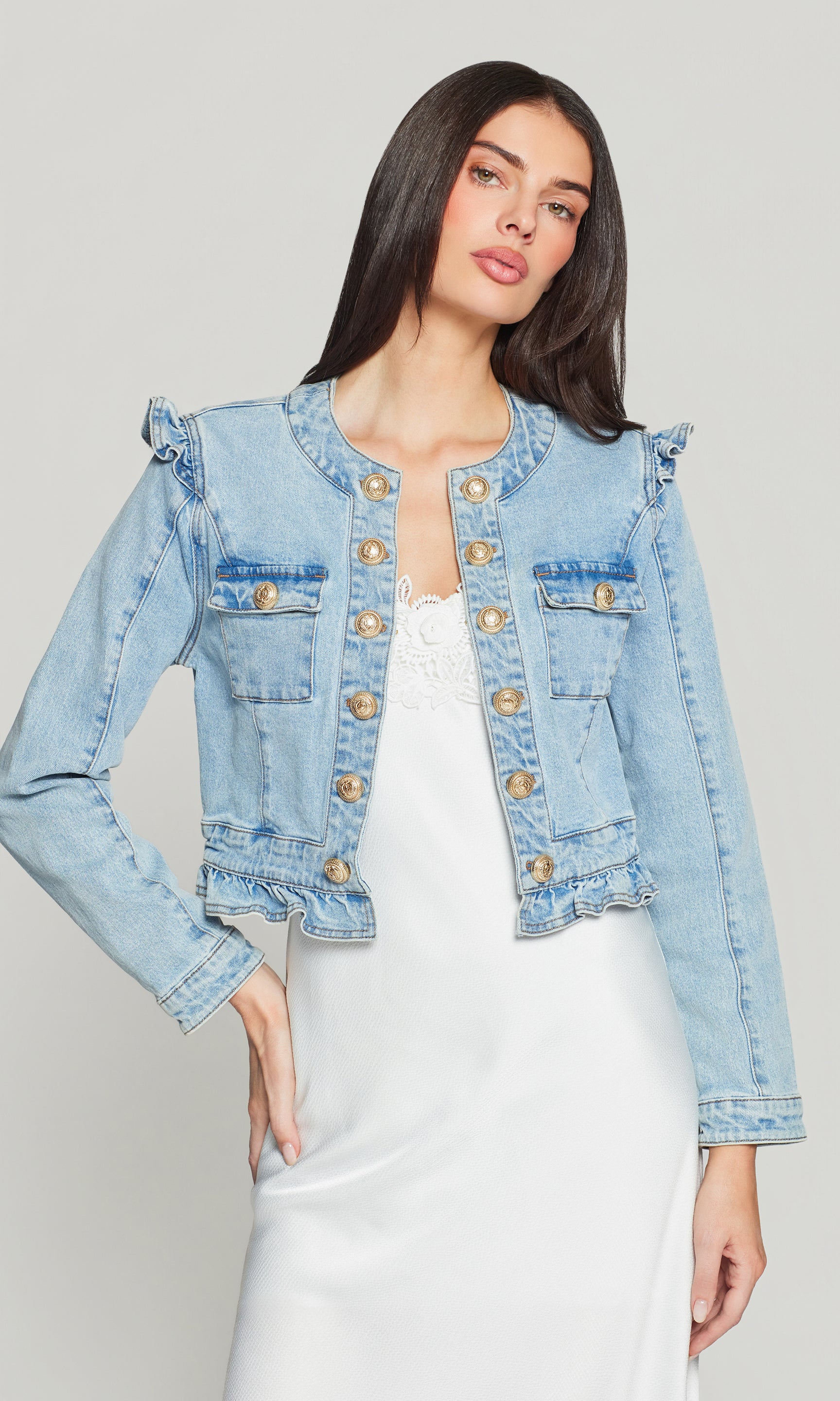 Woman wearing a light blue denim jacket with decorative gold buttons on a gray background