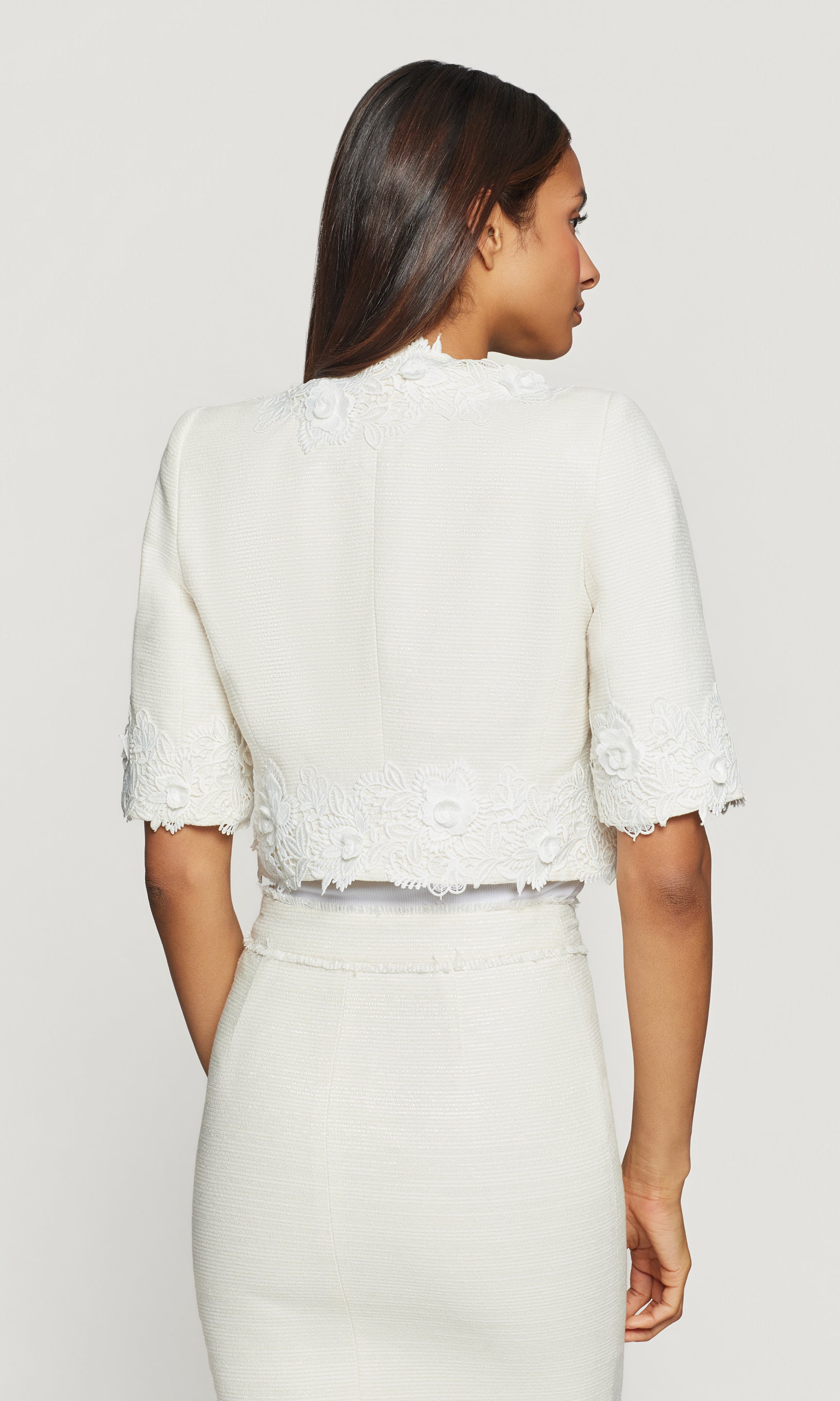 Woman wearing a white lace jacket and skirt set on a plain background
