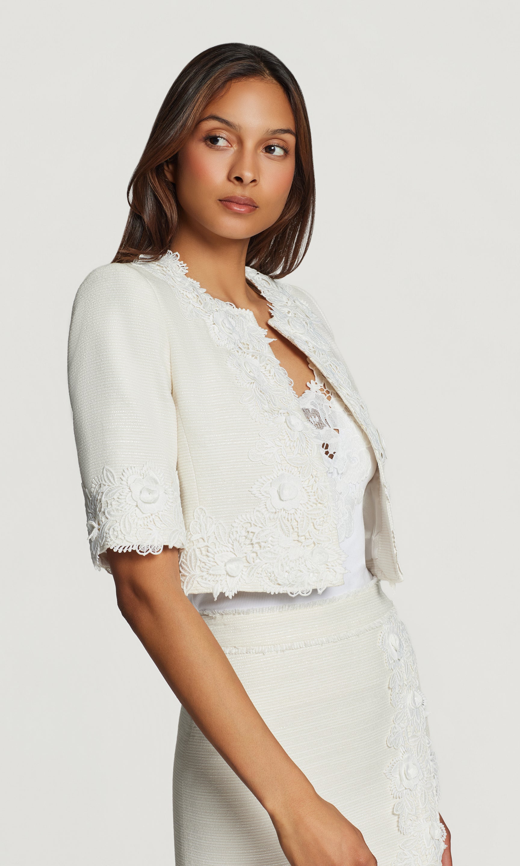 Side view of woman wearing a white lace jacket and skirt set on a plain background