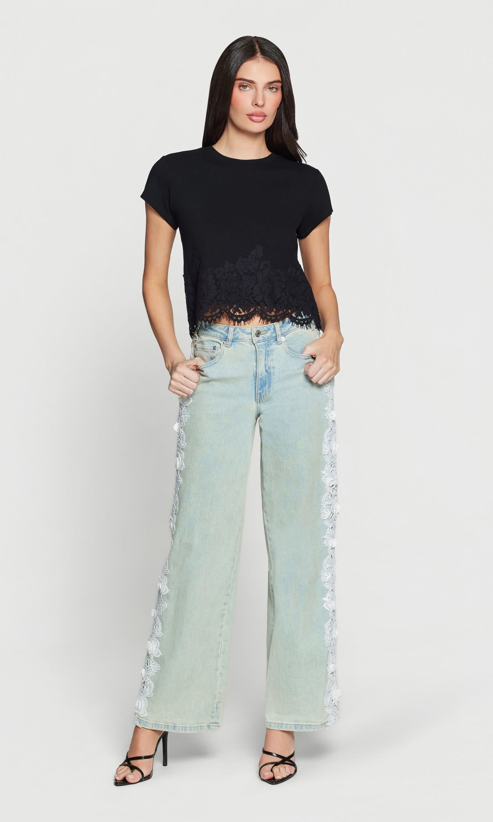 Woman wearing a black top and light blue jeans with lace details on a white background