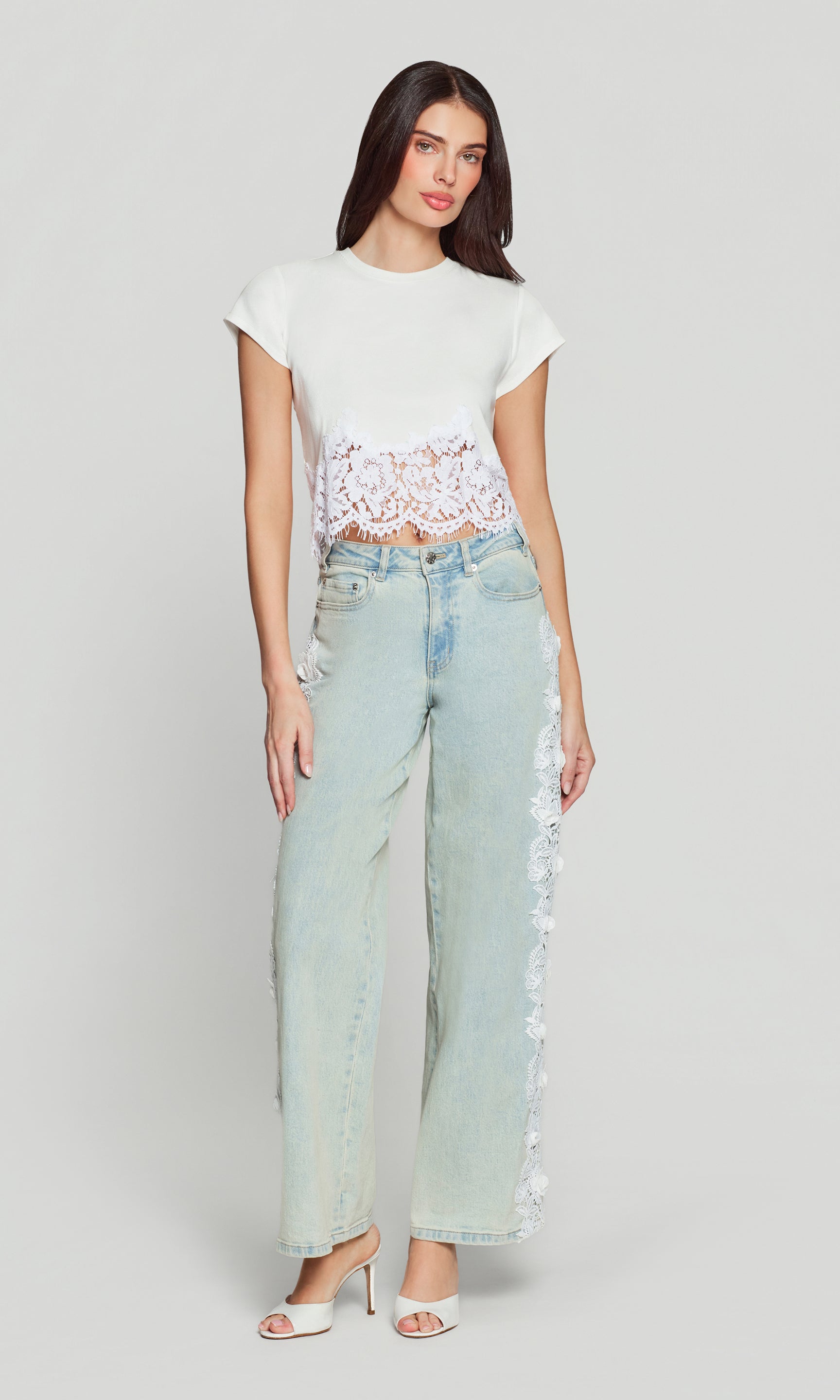 Woman wearing a white lace top and light blue jeans on a plain background