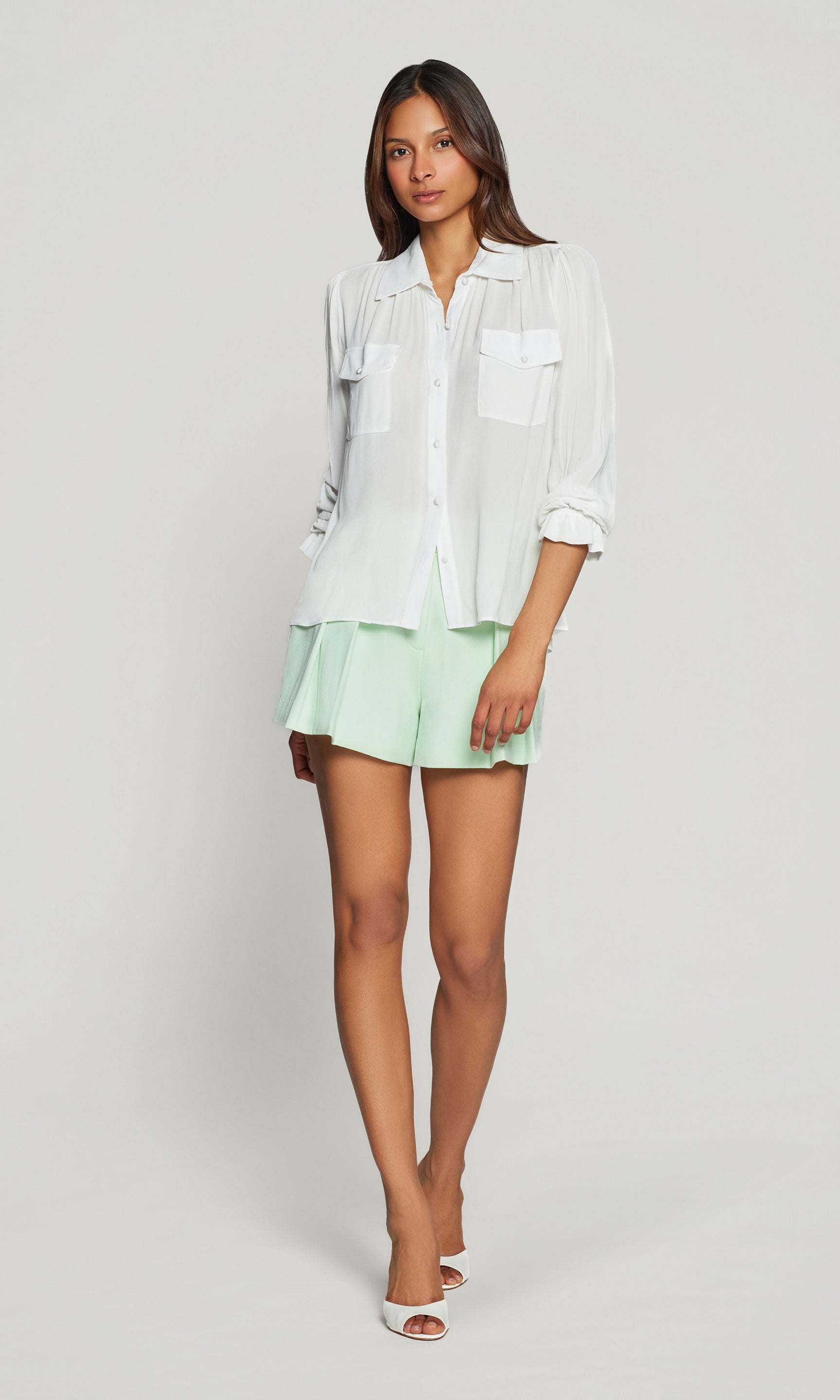 Model wears the Priya Georgette Shirt in white in a full-body view, showing the easy long-sleeve fit and how the hem sits when styled with shorts