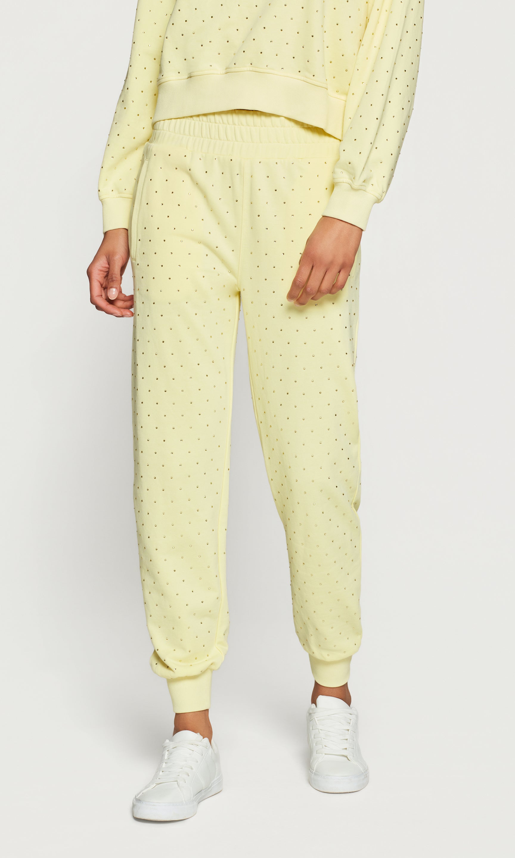 Person wearing a light yellow textured tracksuit with white sneakers on a white background