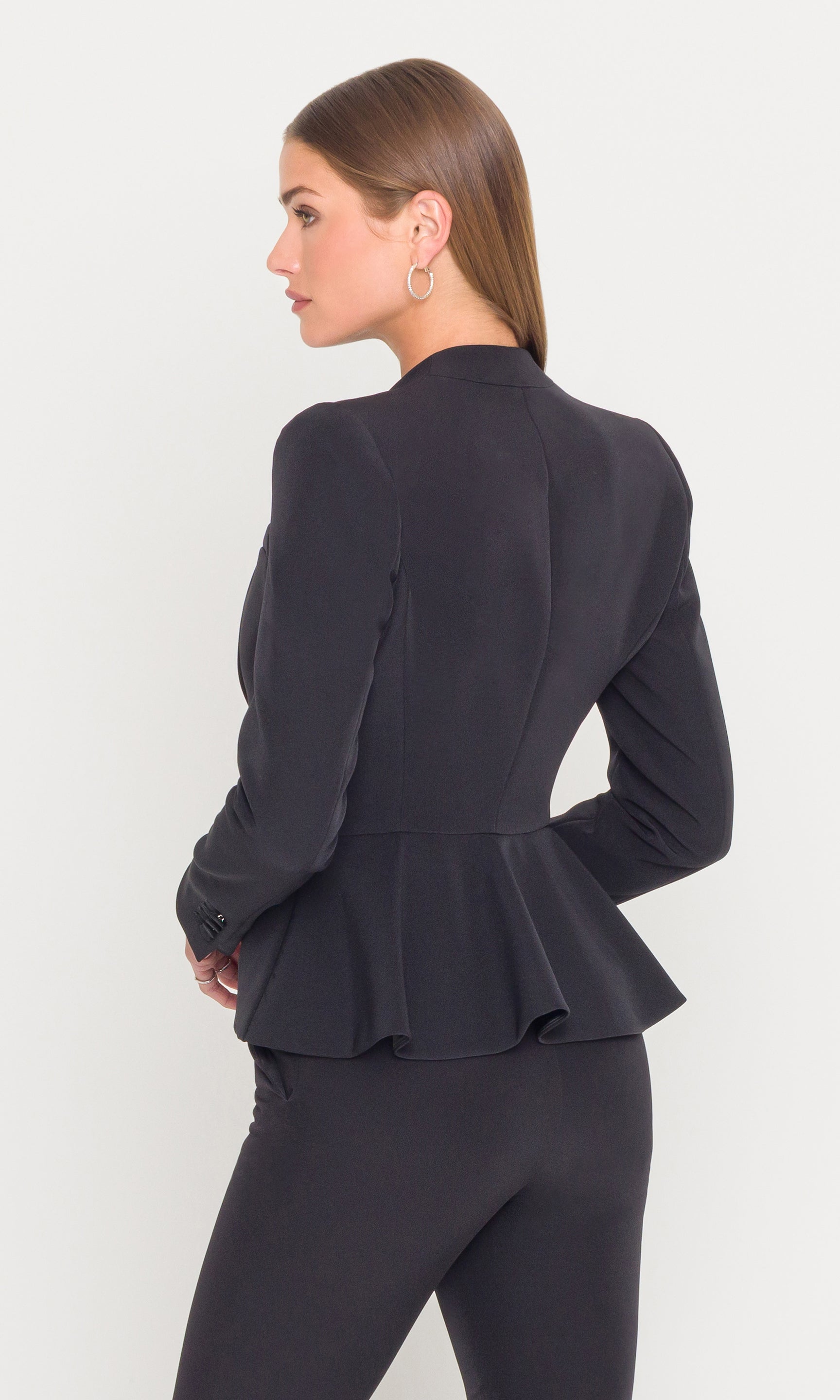Back view of woman wearing a black peplum jacket on a white background
