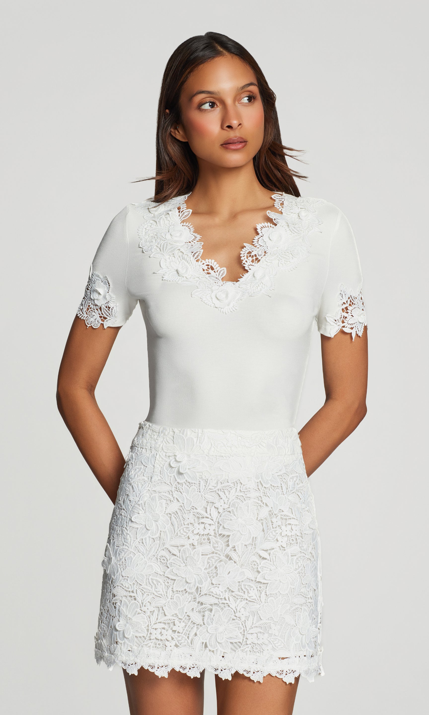 In a three-quarter front view, the model wears the Shiloh 3D Lace Combo Top in white with a white lace mini skirt, highlighting the lace neckline and sleeve detail.