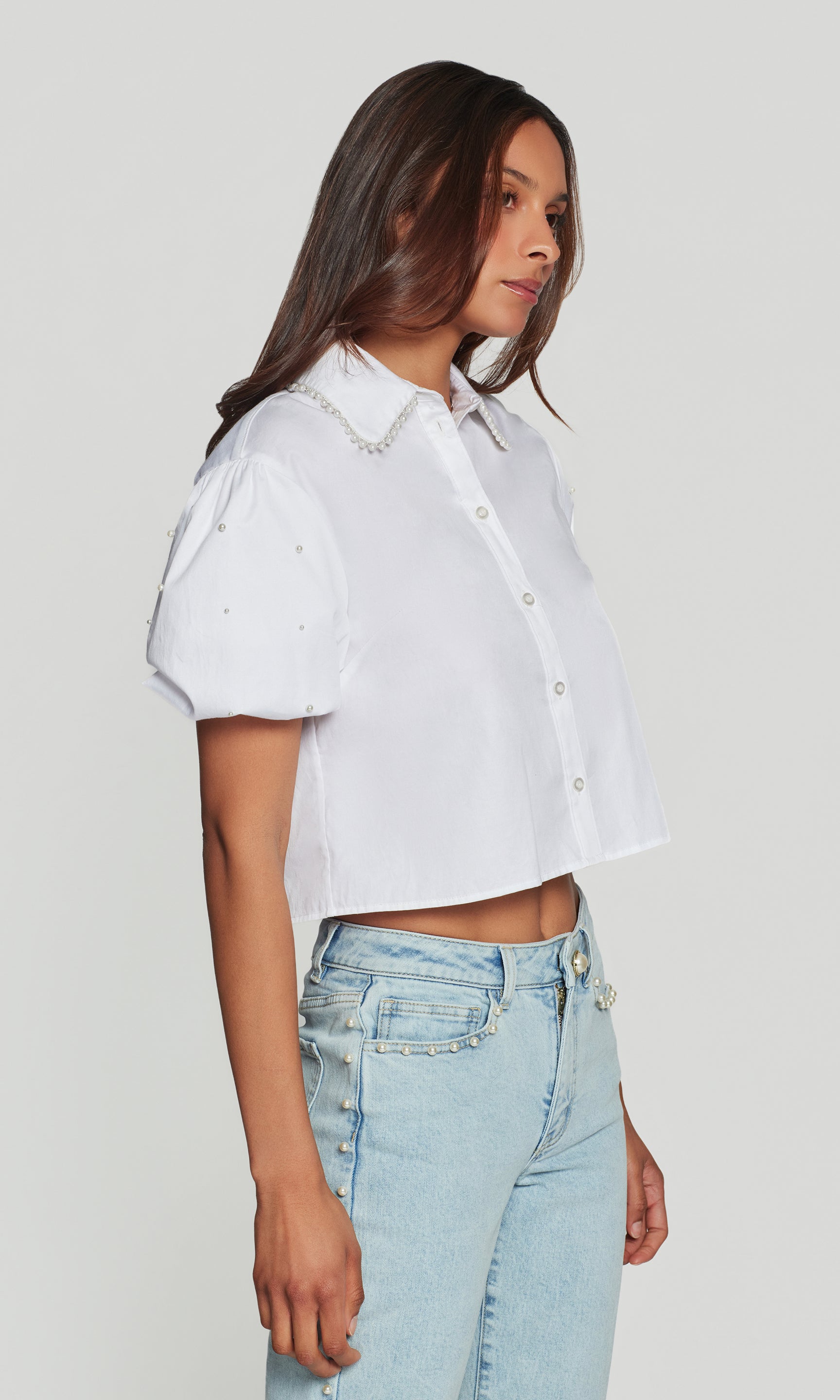 In a studio side view, the model wears the Soo Pearl Poplin Shirt in white, showing the cropped hem and sleeve volume from the profile.