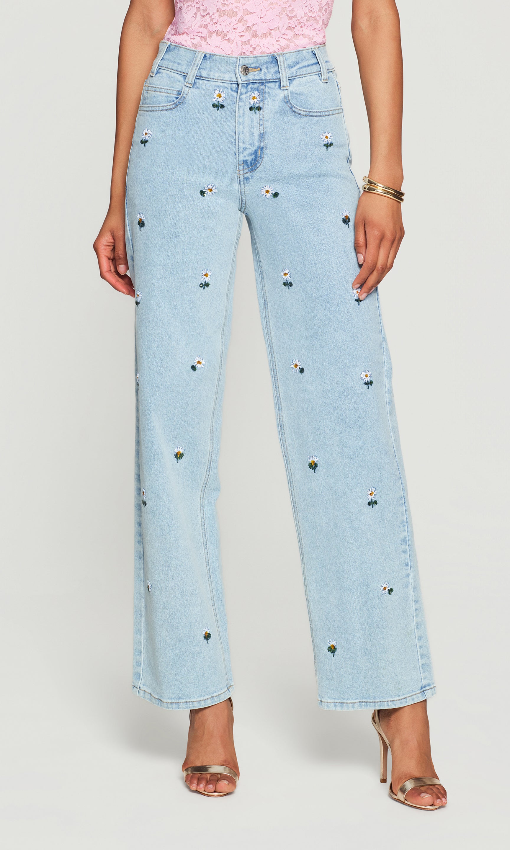 Light blue jeans with decorative flower patterns worn by a person on a white background