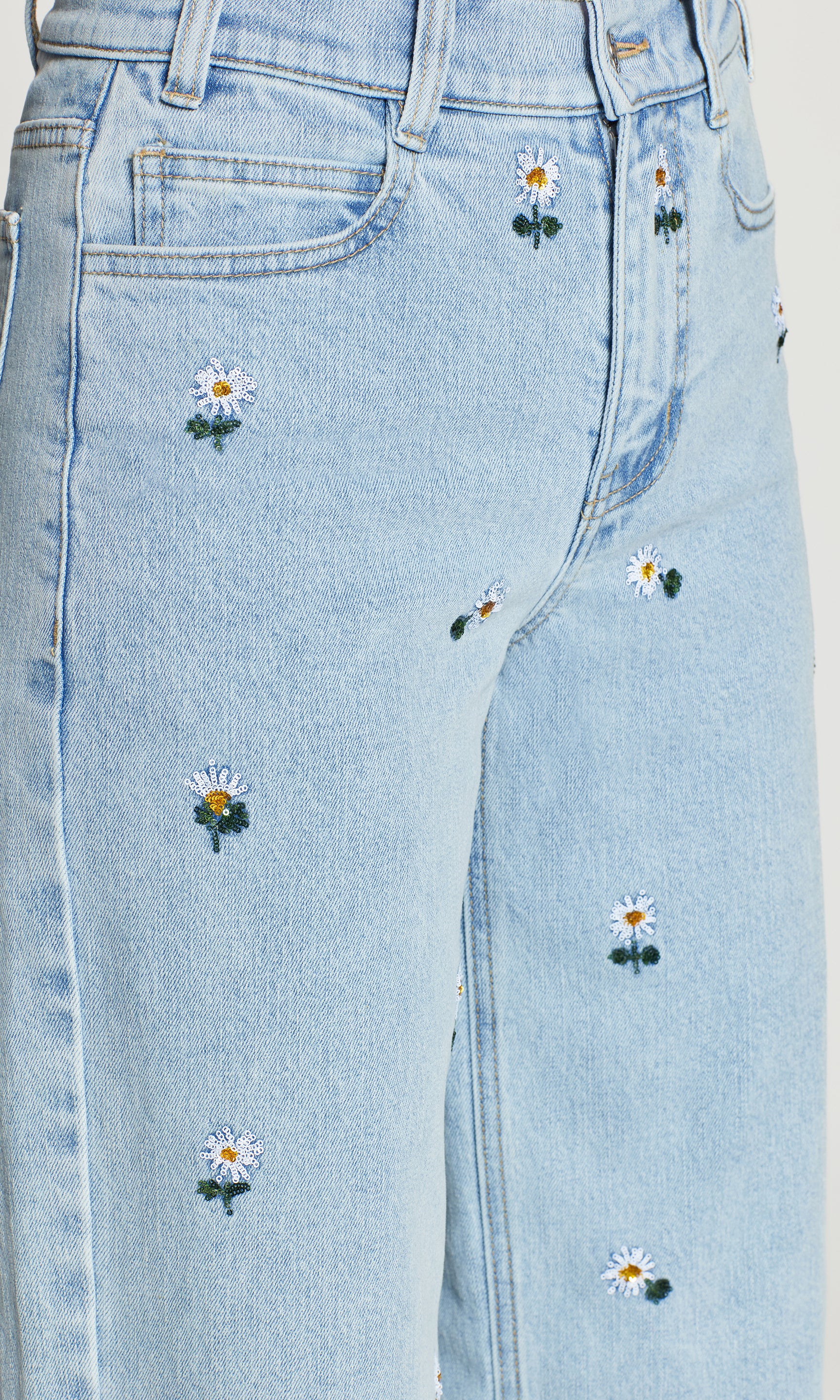 Close-up of light blue jeans with floral embroidery on a plain background