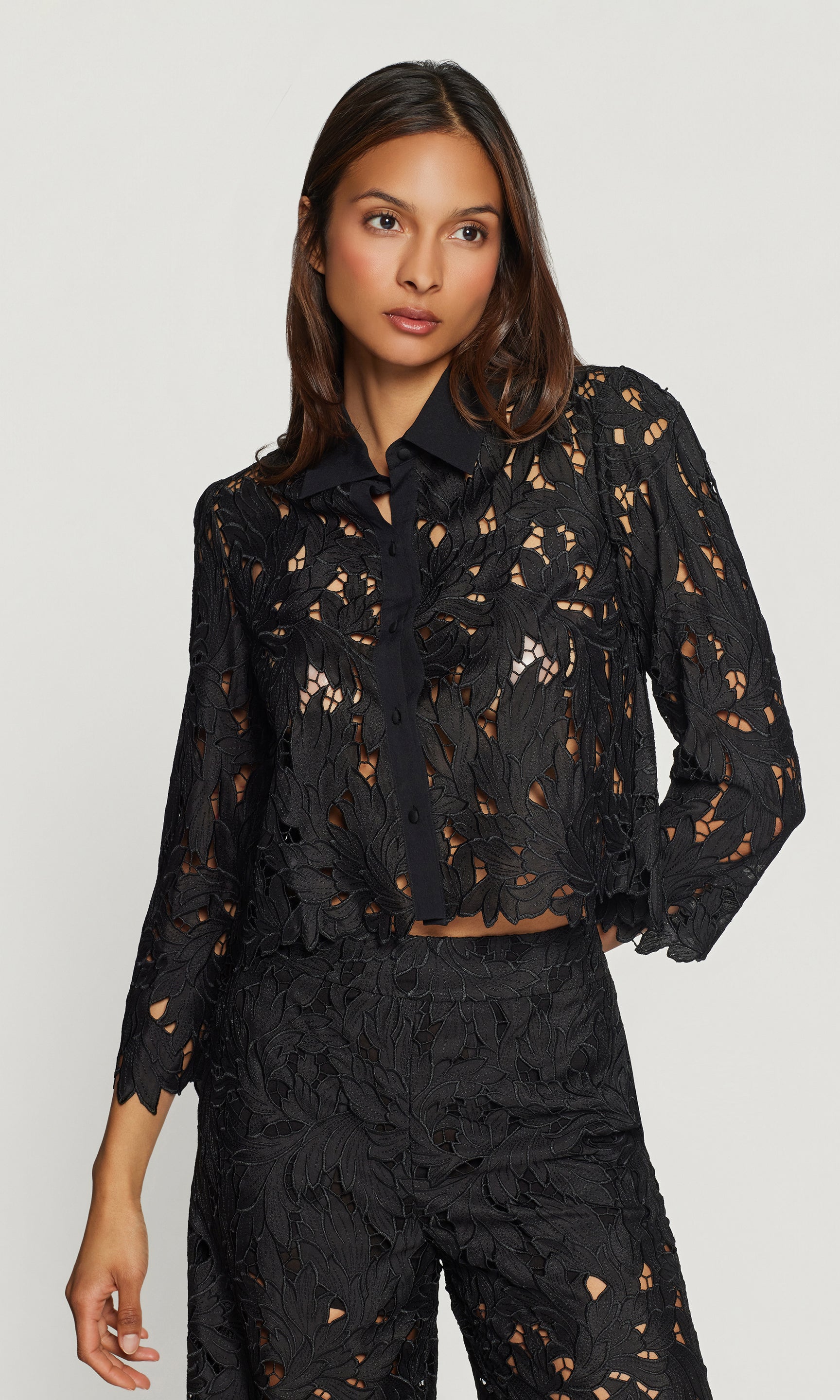 Woman wearing a black floral blouse and pants on a plain background