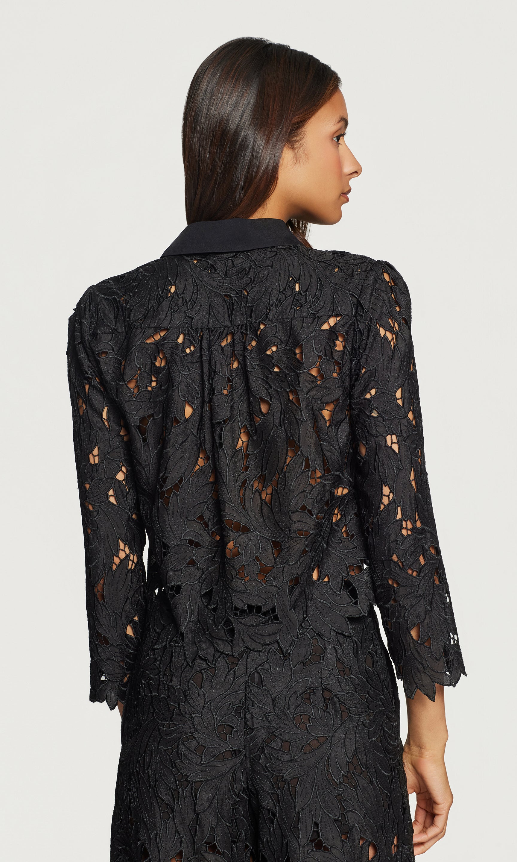 Back view of woman wearing a black lace top with a plain background