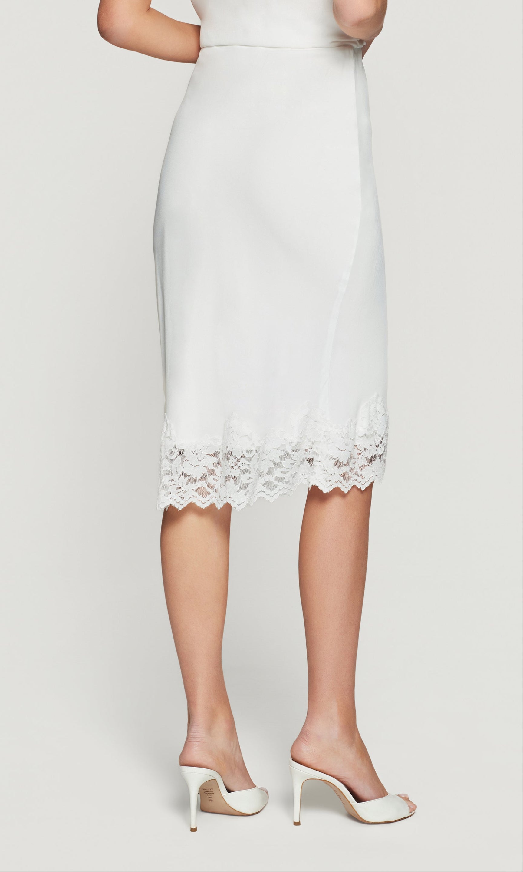 Back view of white pencil skirt with lace hem on a plain background
