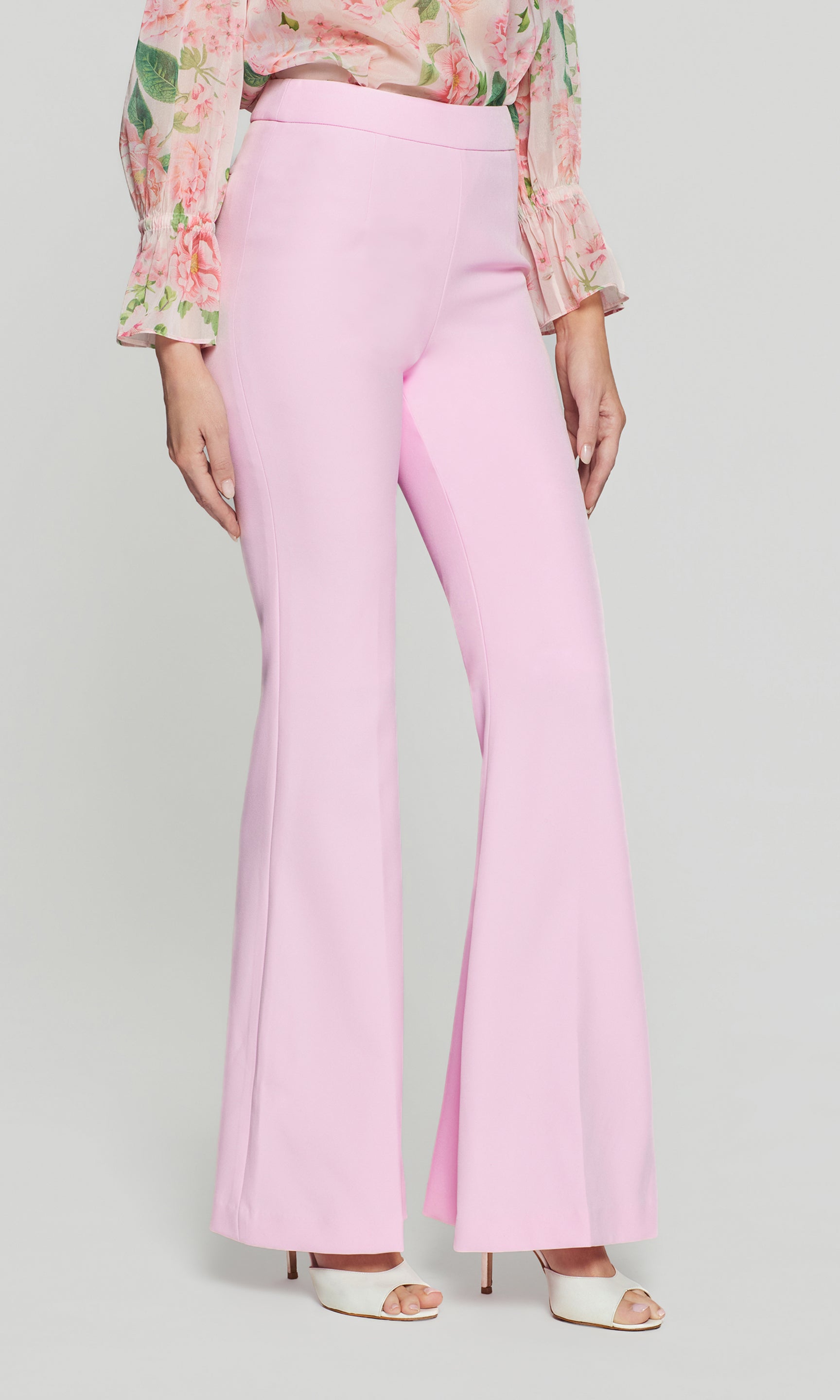 Side view of person wearing pink flared pants with a floral blouse on a light gray background