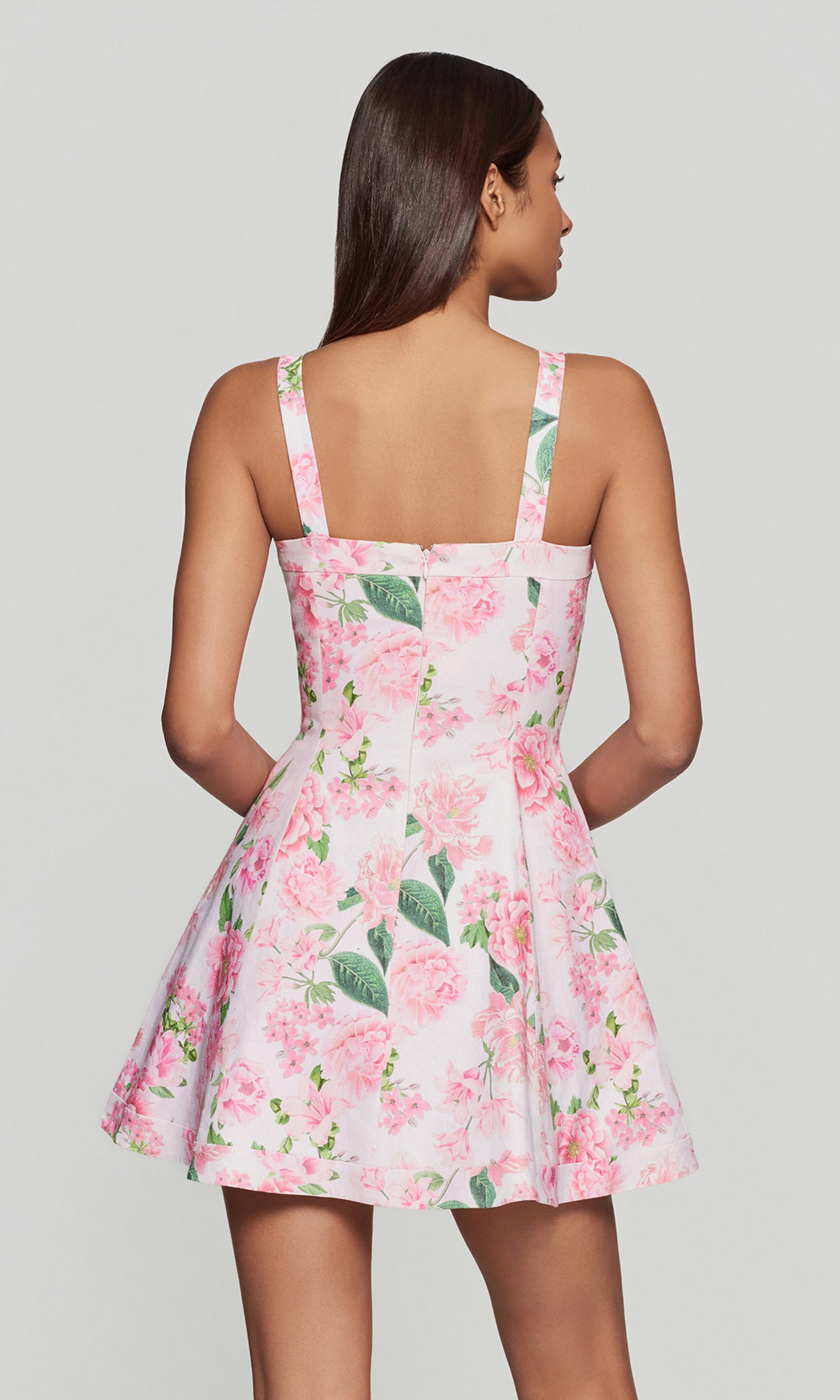 Back view of woman wearing a floral dress with pink flowers and green leaves on a plain background
