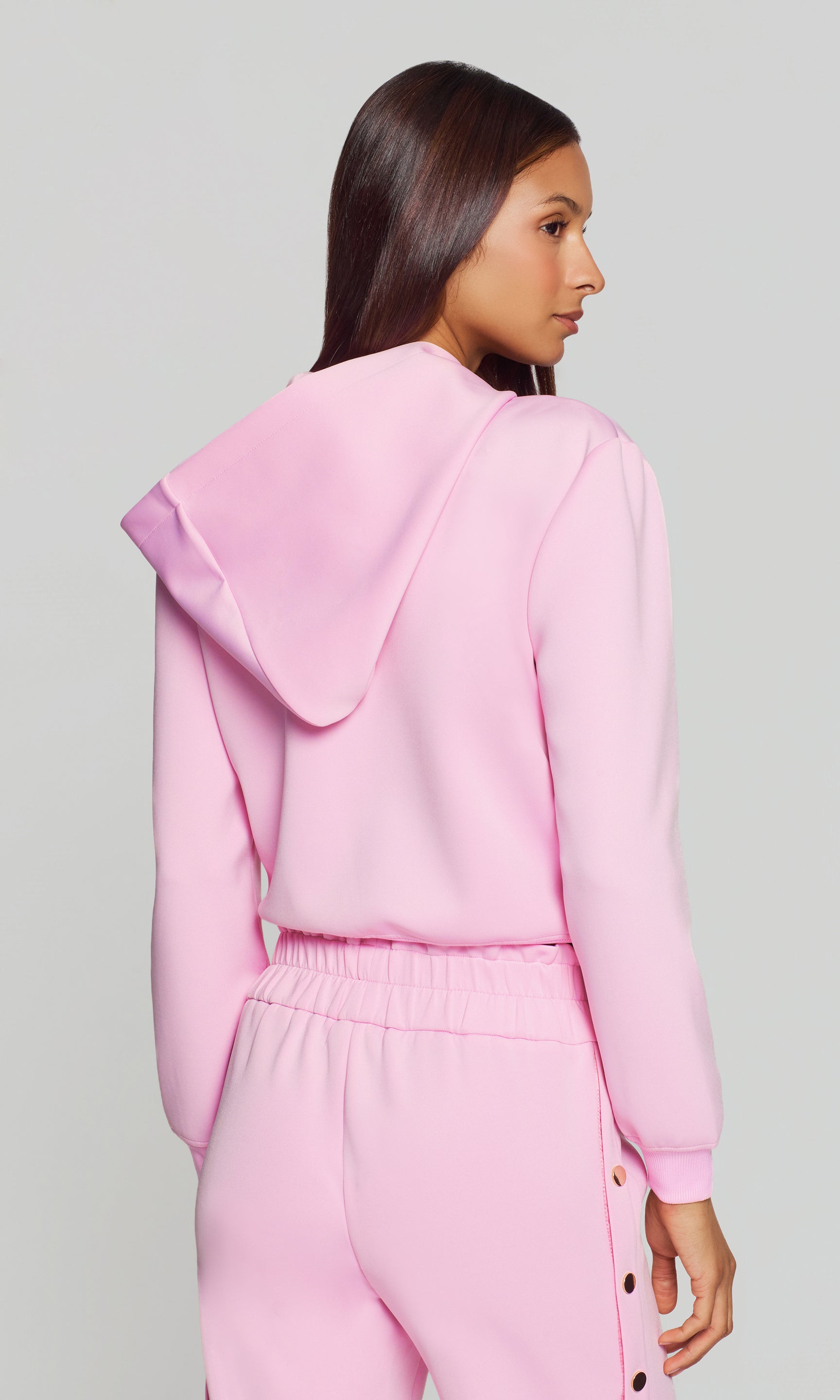 Back view of person wearing a pink hoodie and pants set on a gray background