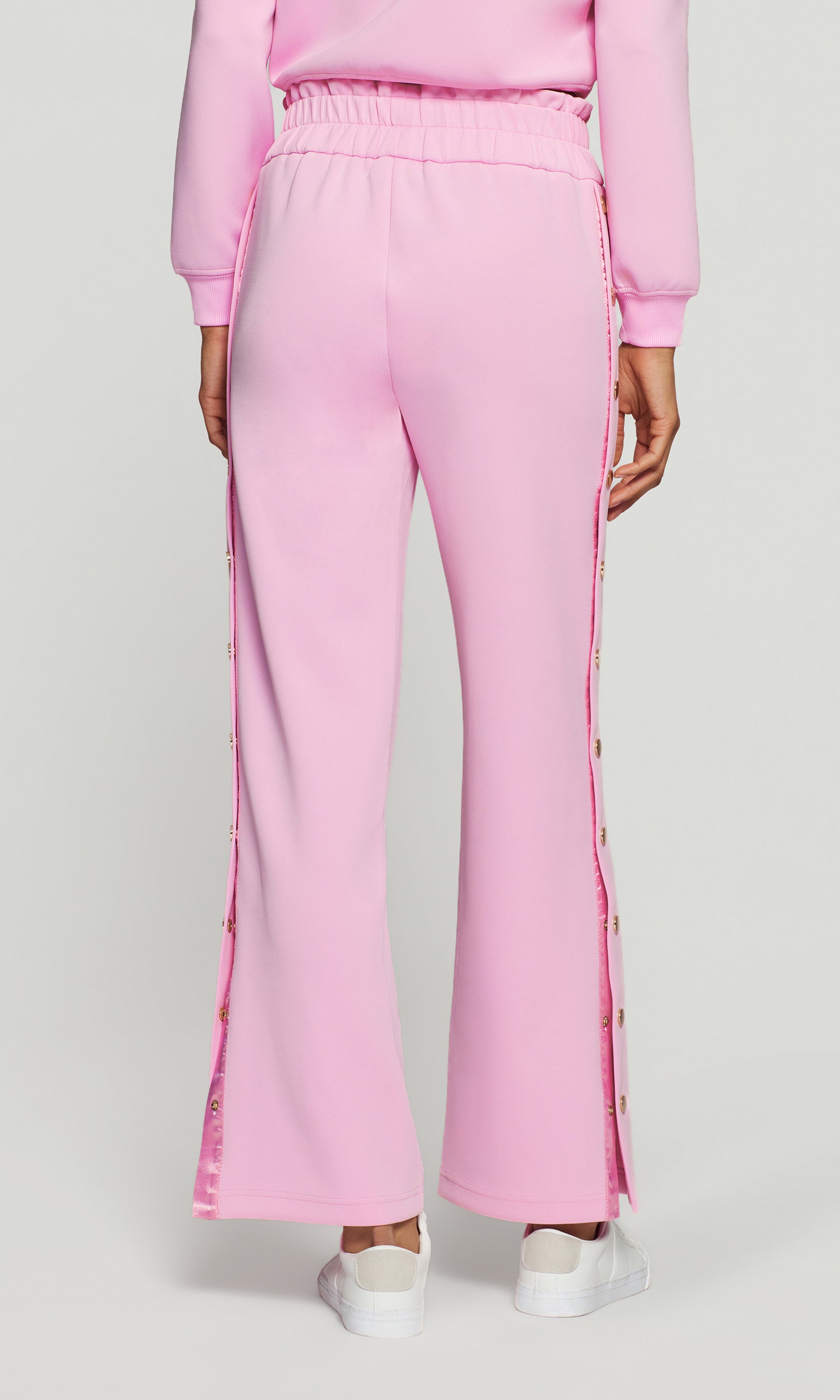 Back view of pink tracksuit pants with side buttons on a white background