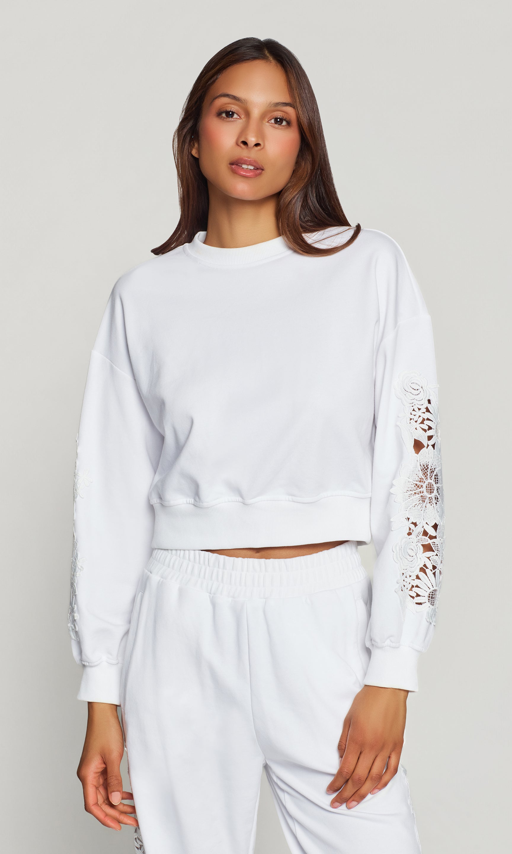 Woman wearing a white sweatshirt with lace sleeves on a plain background