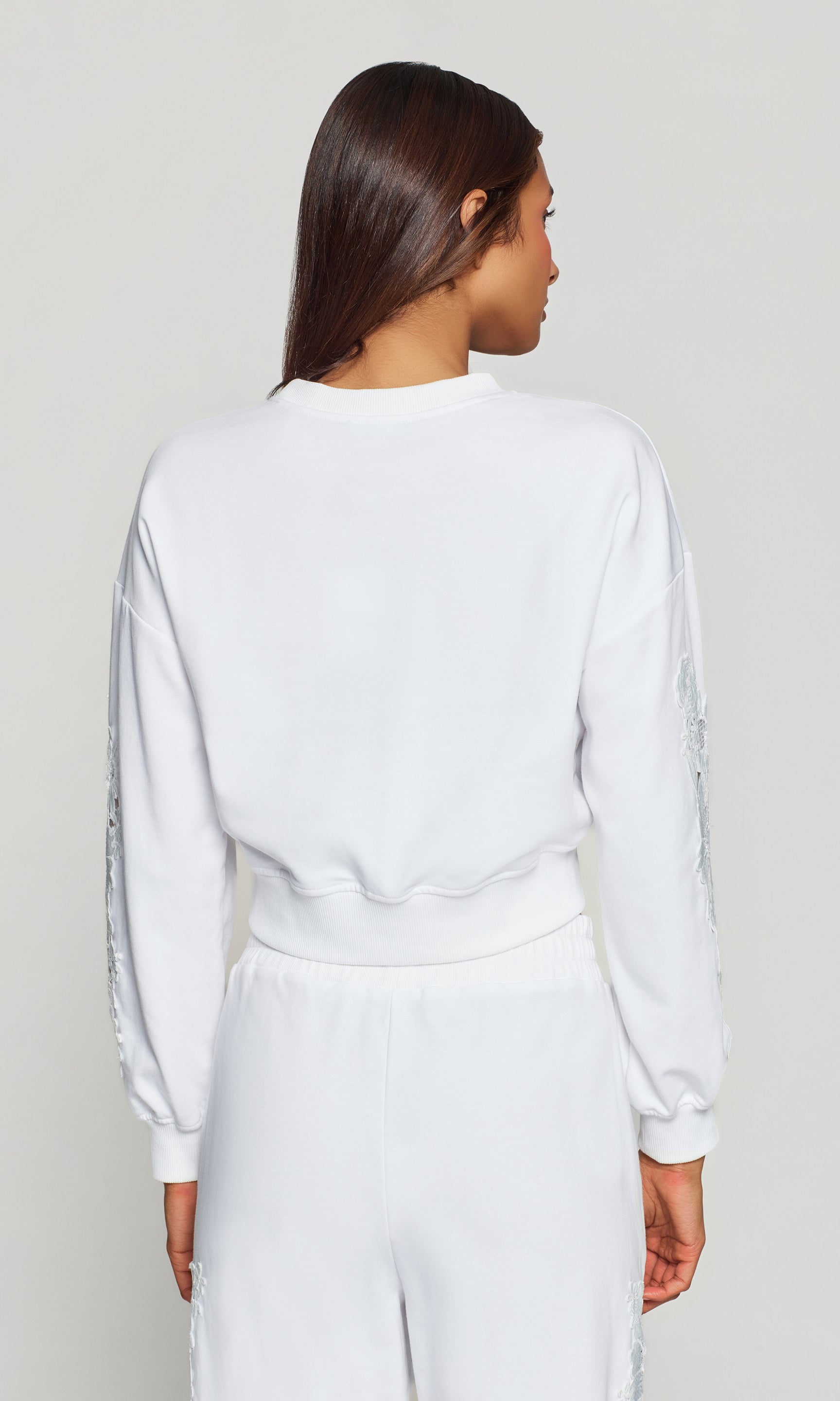 Back view of person wearing a white sweatshirt and pants on a plain background