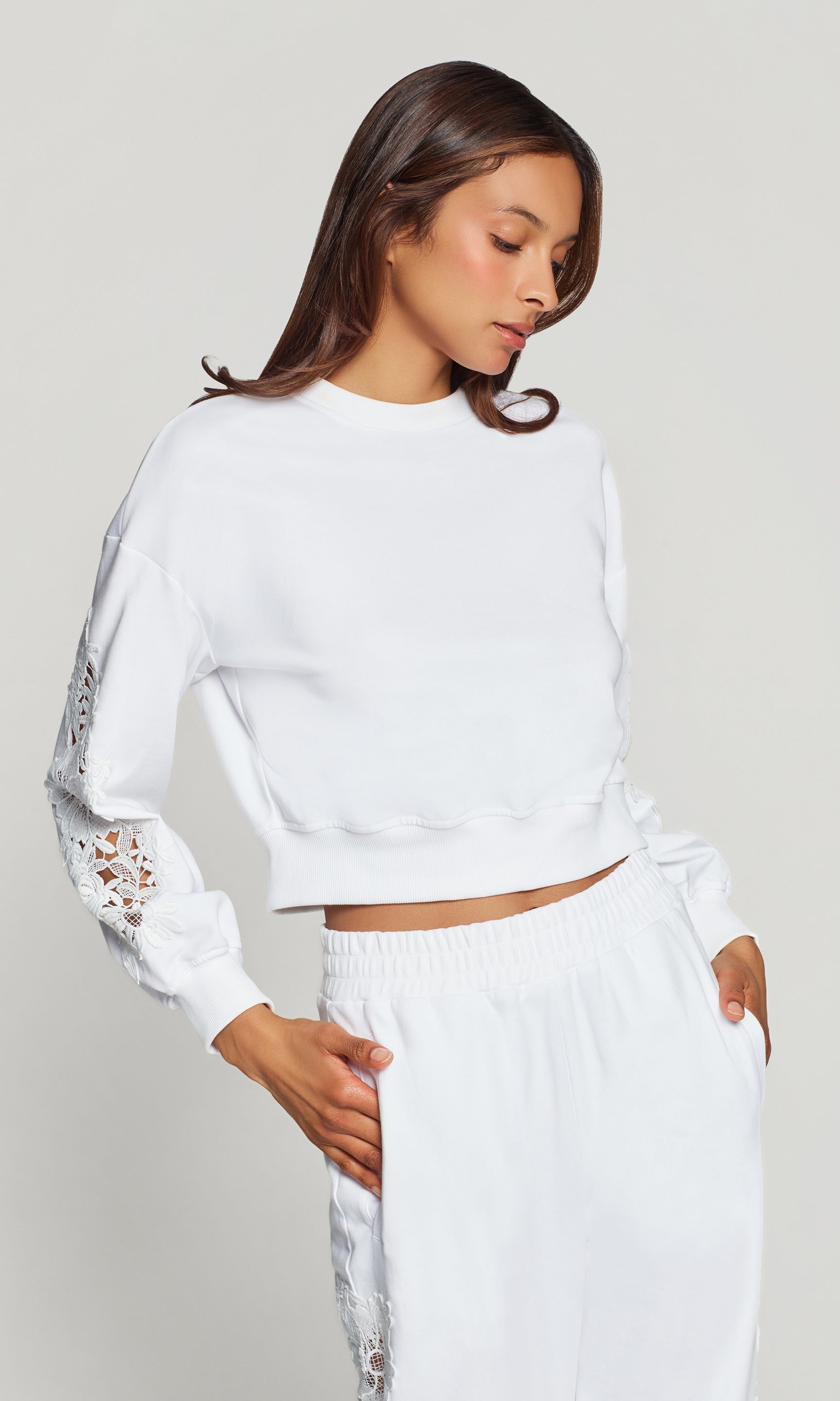 Side view of woman wearing a white sweater with lace sleeves on a plain background