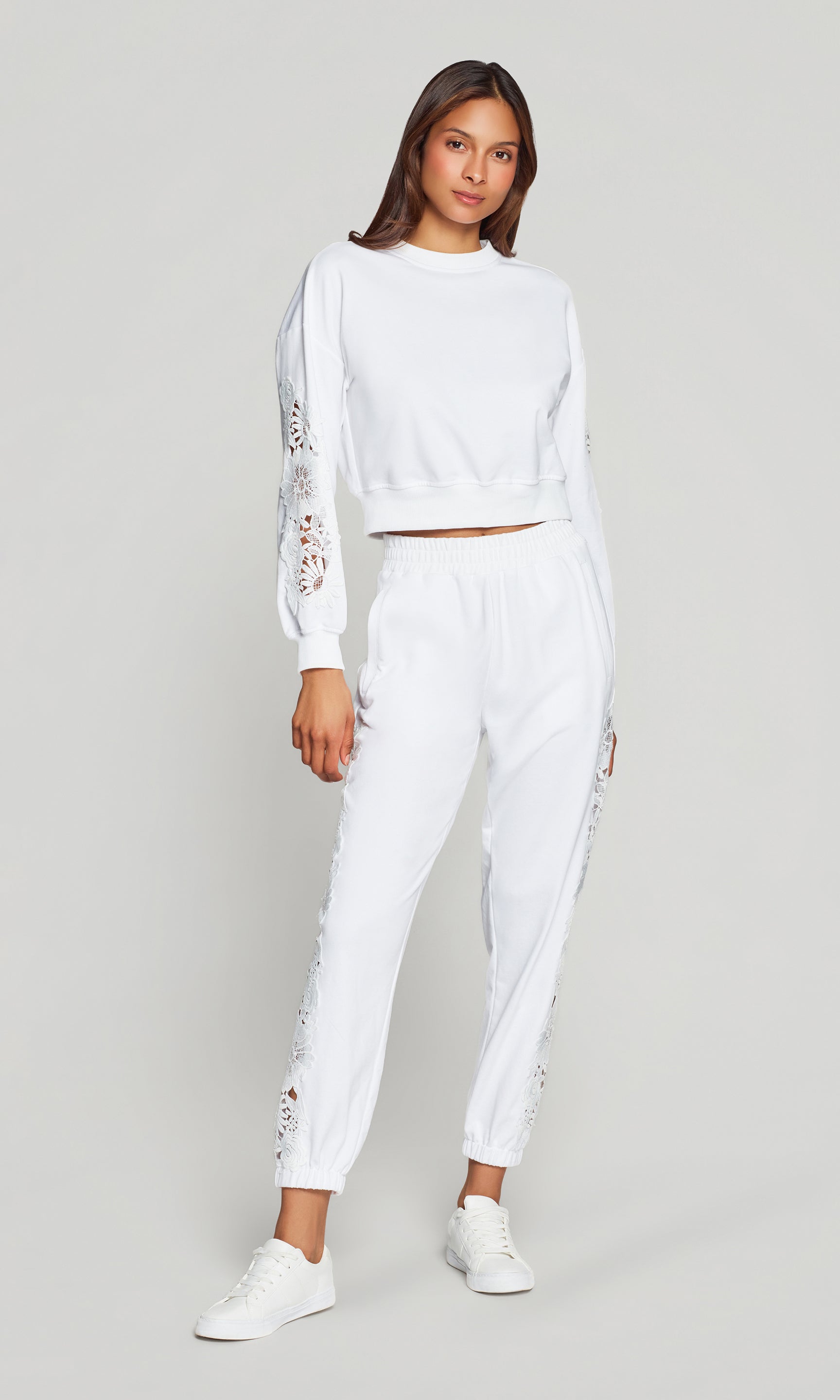 Woman wearing a white outfit with floral lace details on a gray background