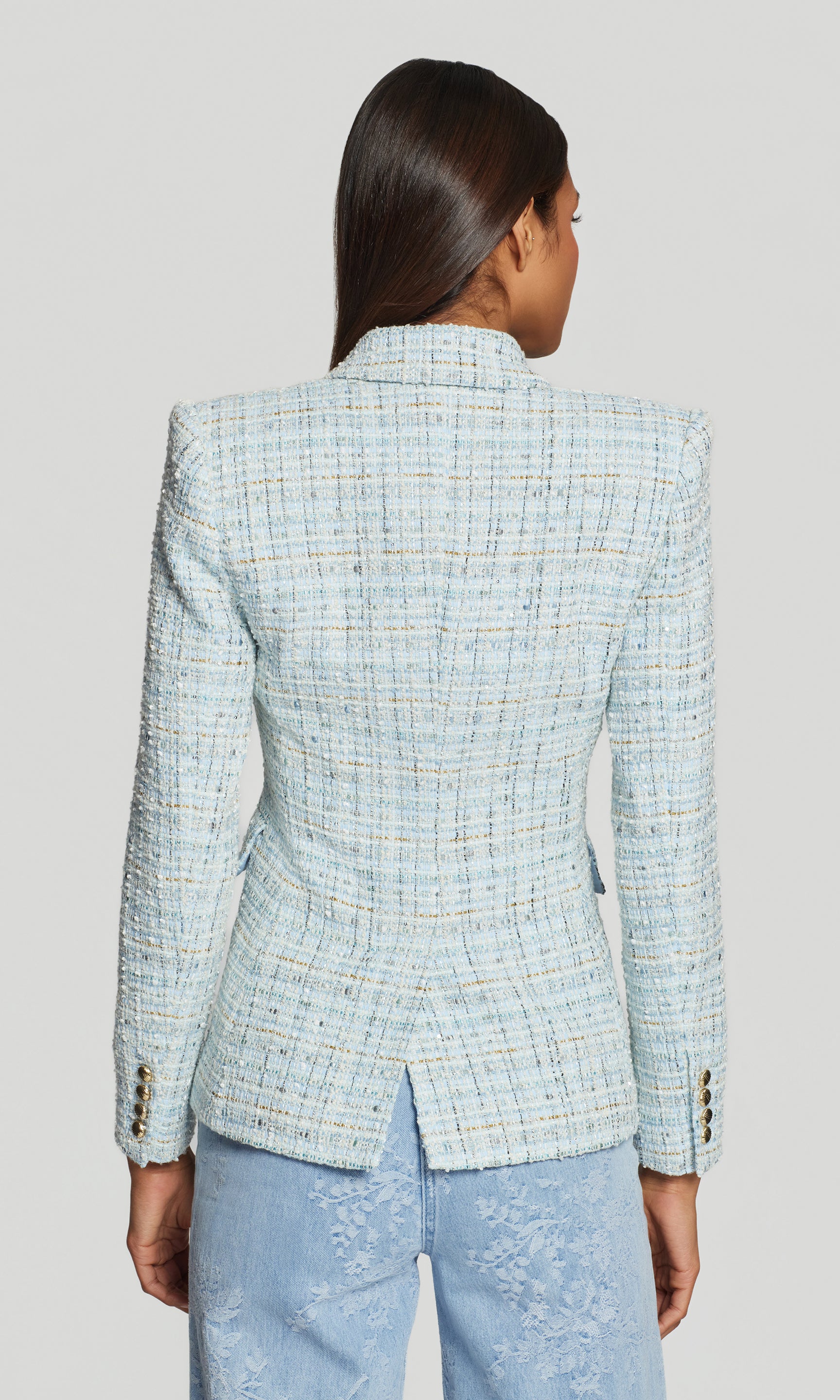 Back view of person wearing a light blue tweed blazer on a gray background