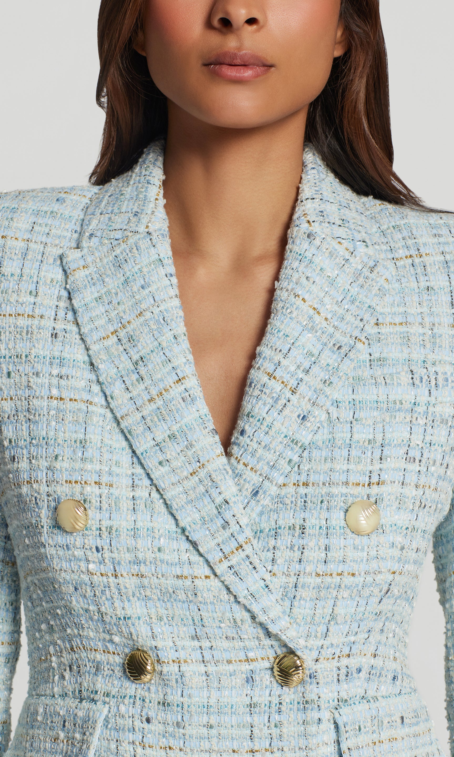 Close-up of light blue tweed blazer with gold buttons worn by a person.
