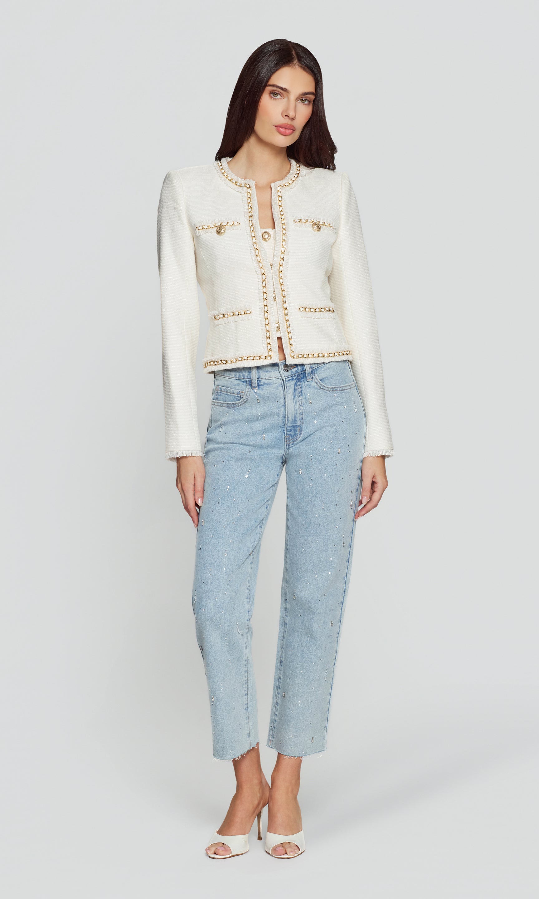 Woman wearing a white jacket with gold accents and light blue jeans on a white background