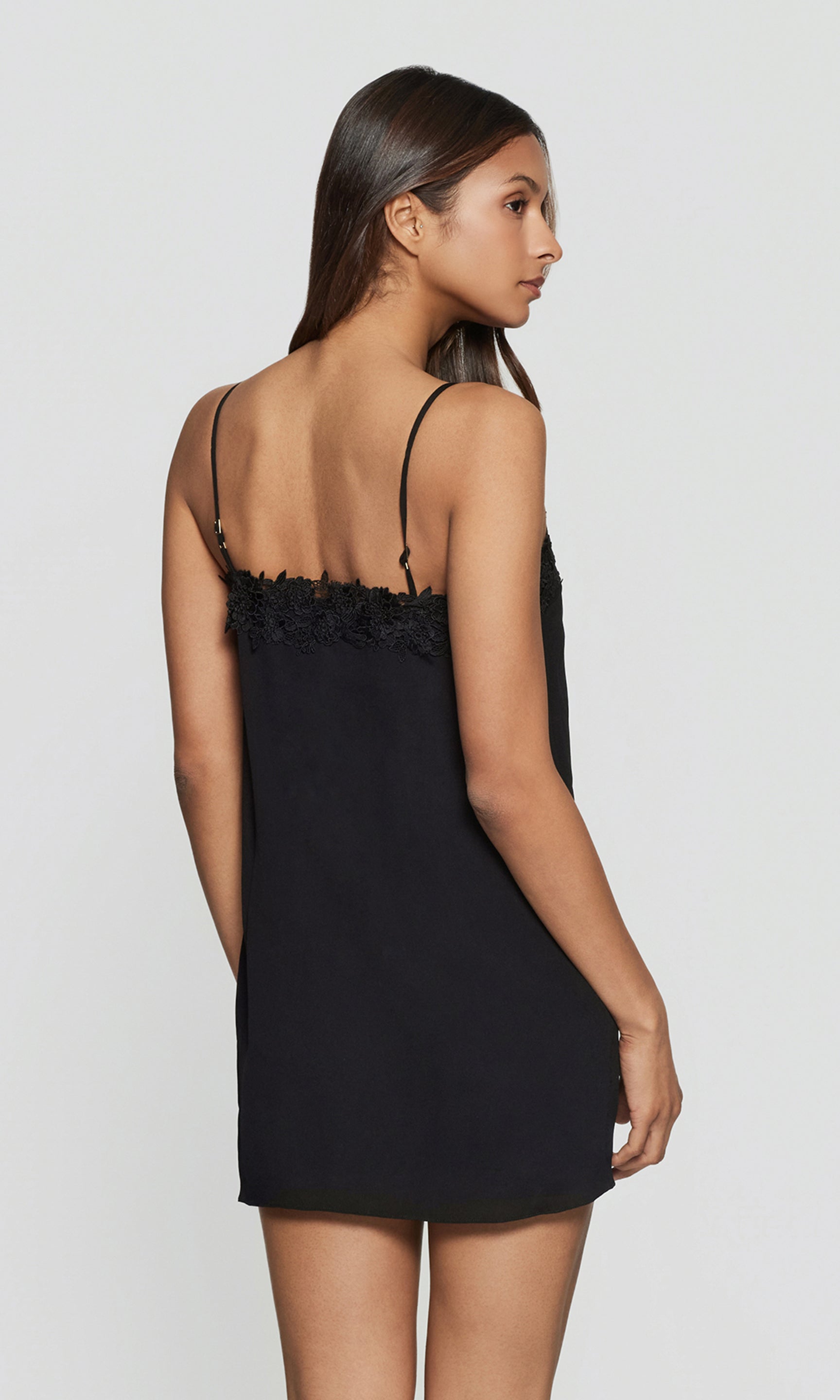 Back view of woman wearing a black slip dress with floral details on a white background