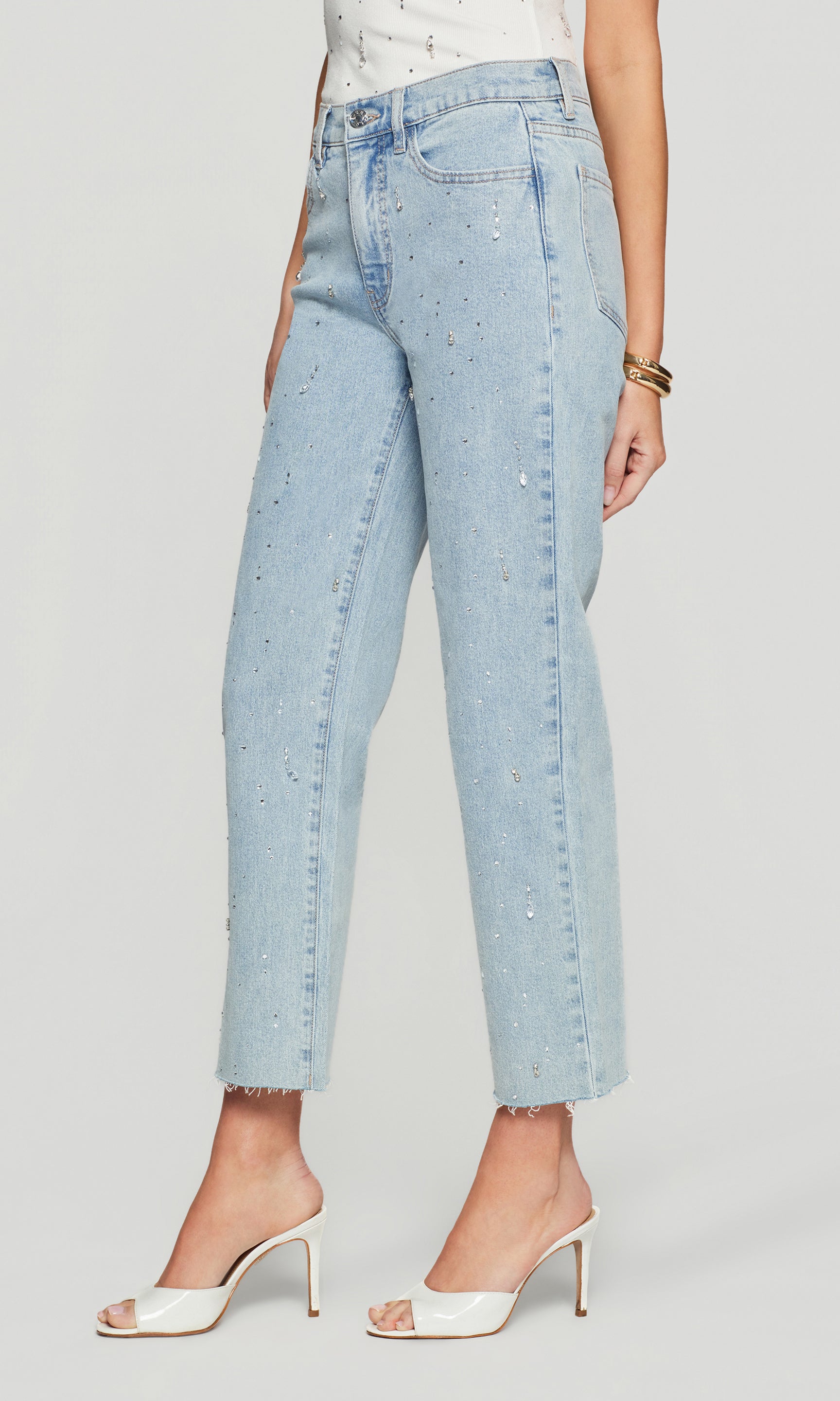 Side view of light blue jeans with crystal embellishments worn by a person on a plain background