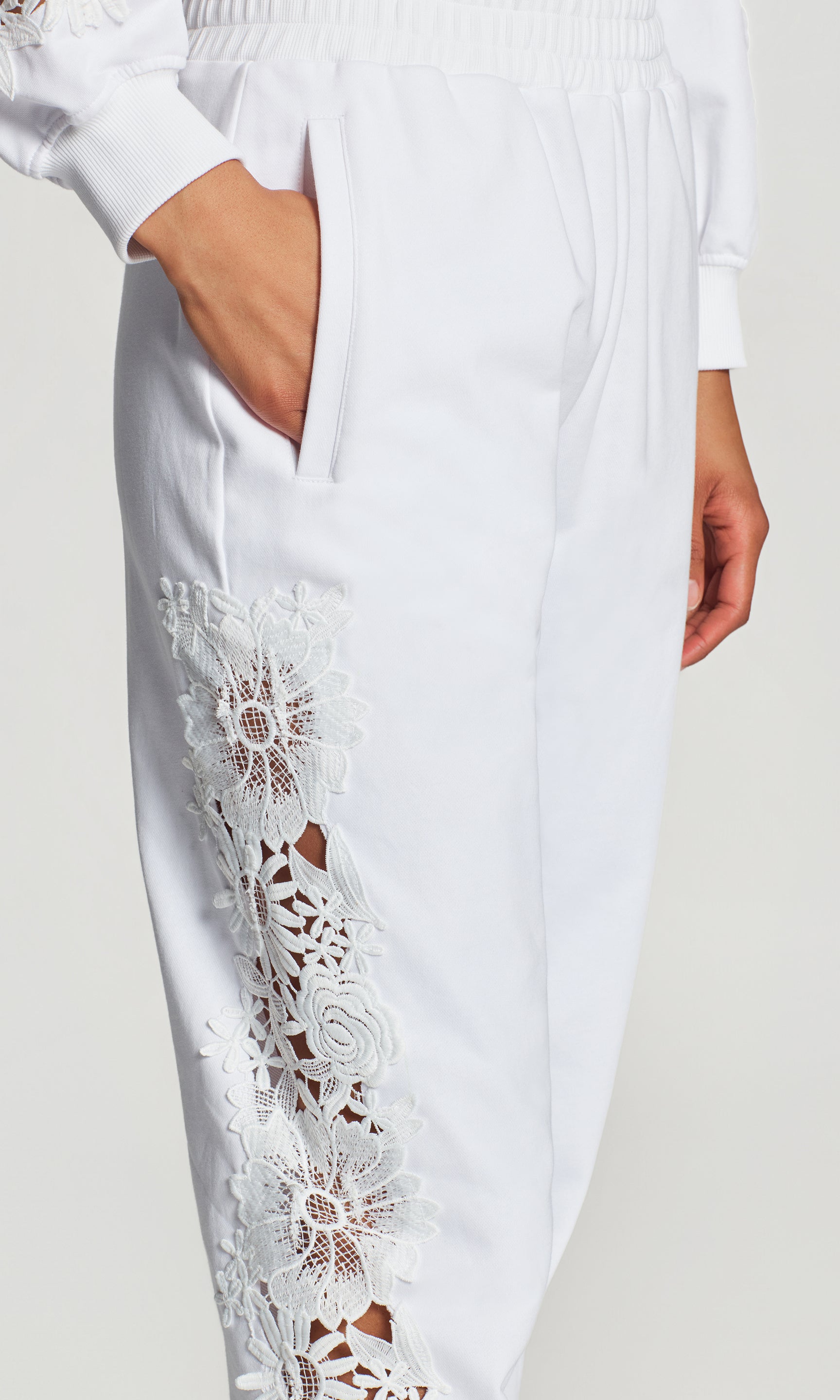 Close-up of white pant with lace detailing on a plain background