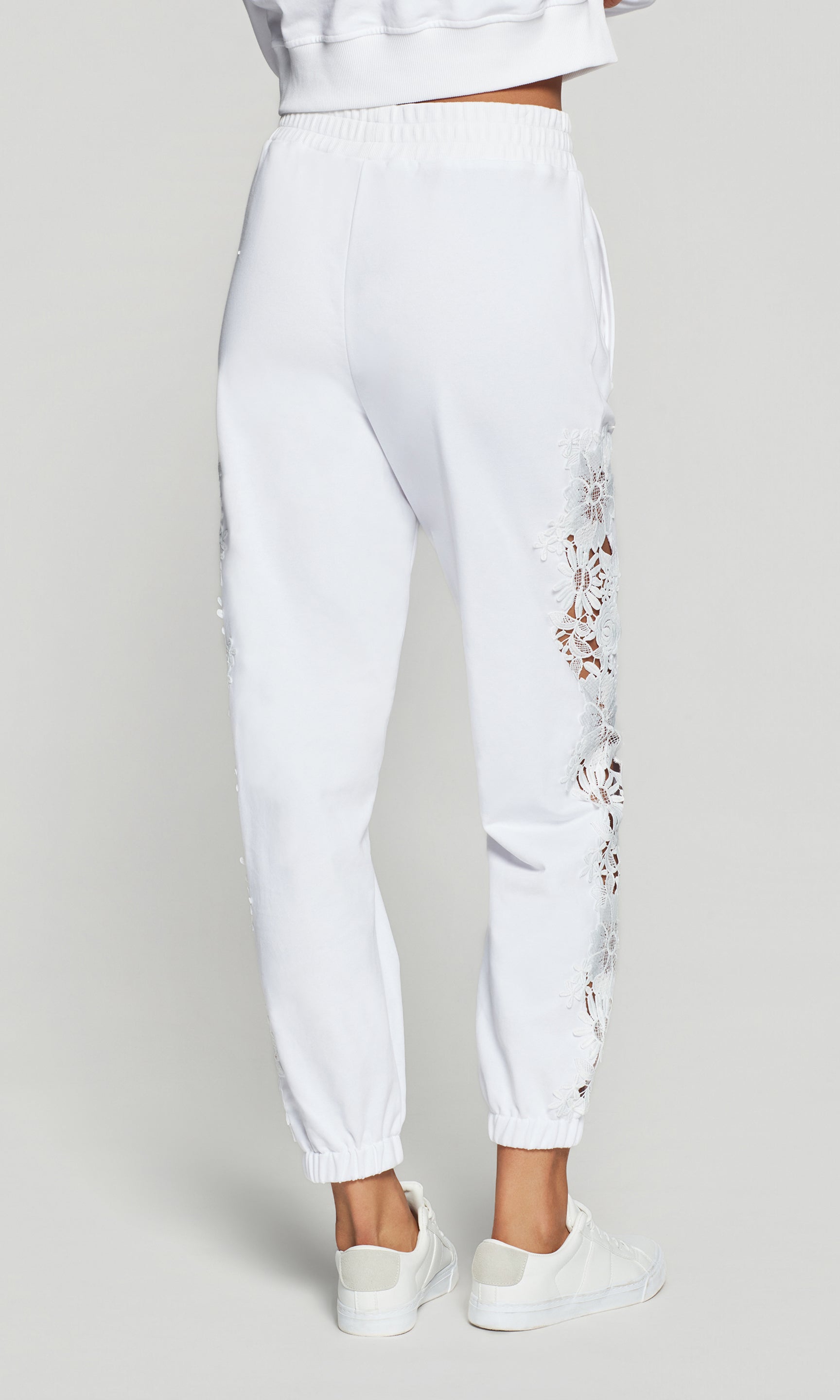 Back view of white jogger pants with floral embroidery on a light gray background