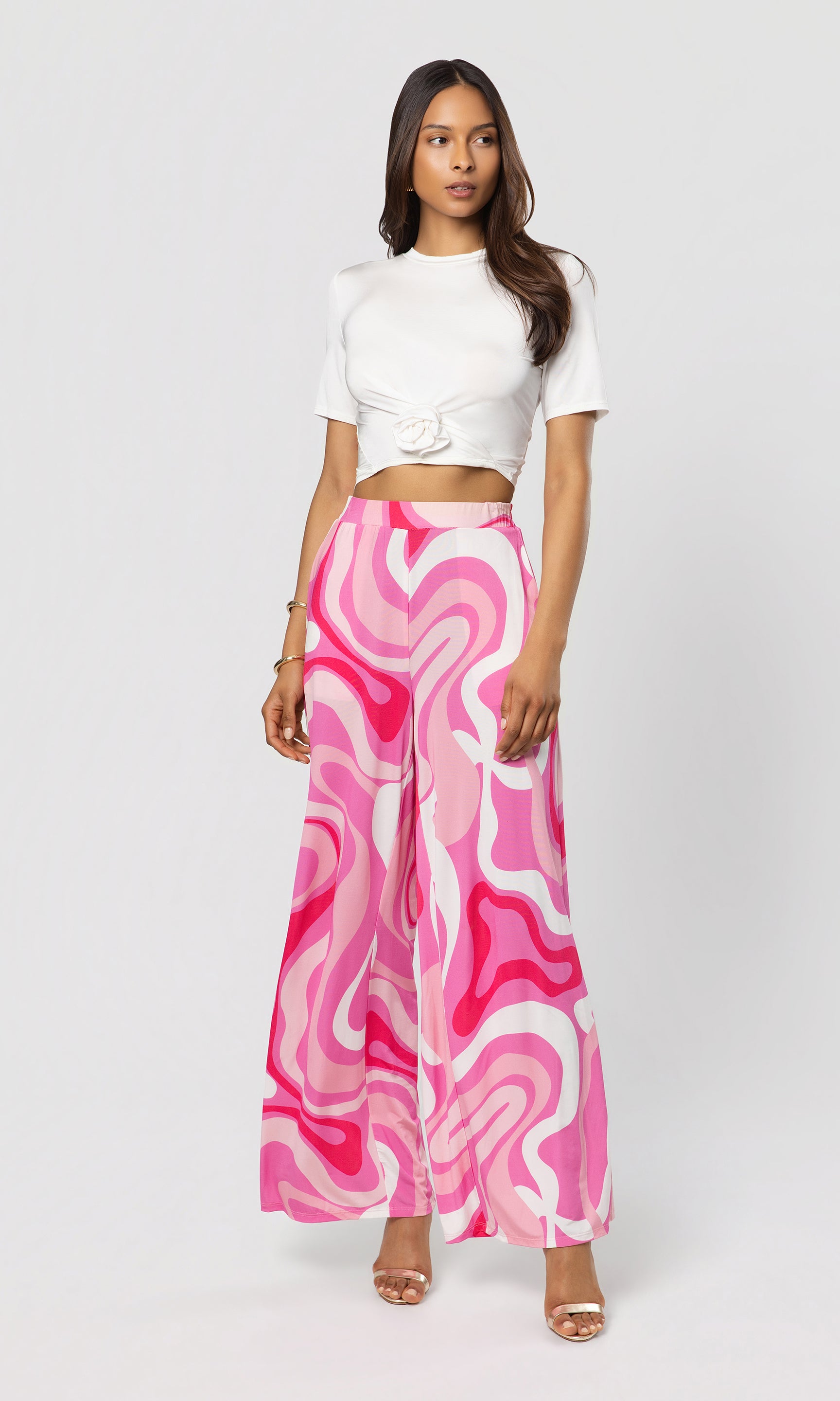 Woman wearing a white top and pink and white patterned pants on a light gray background