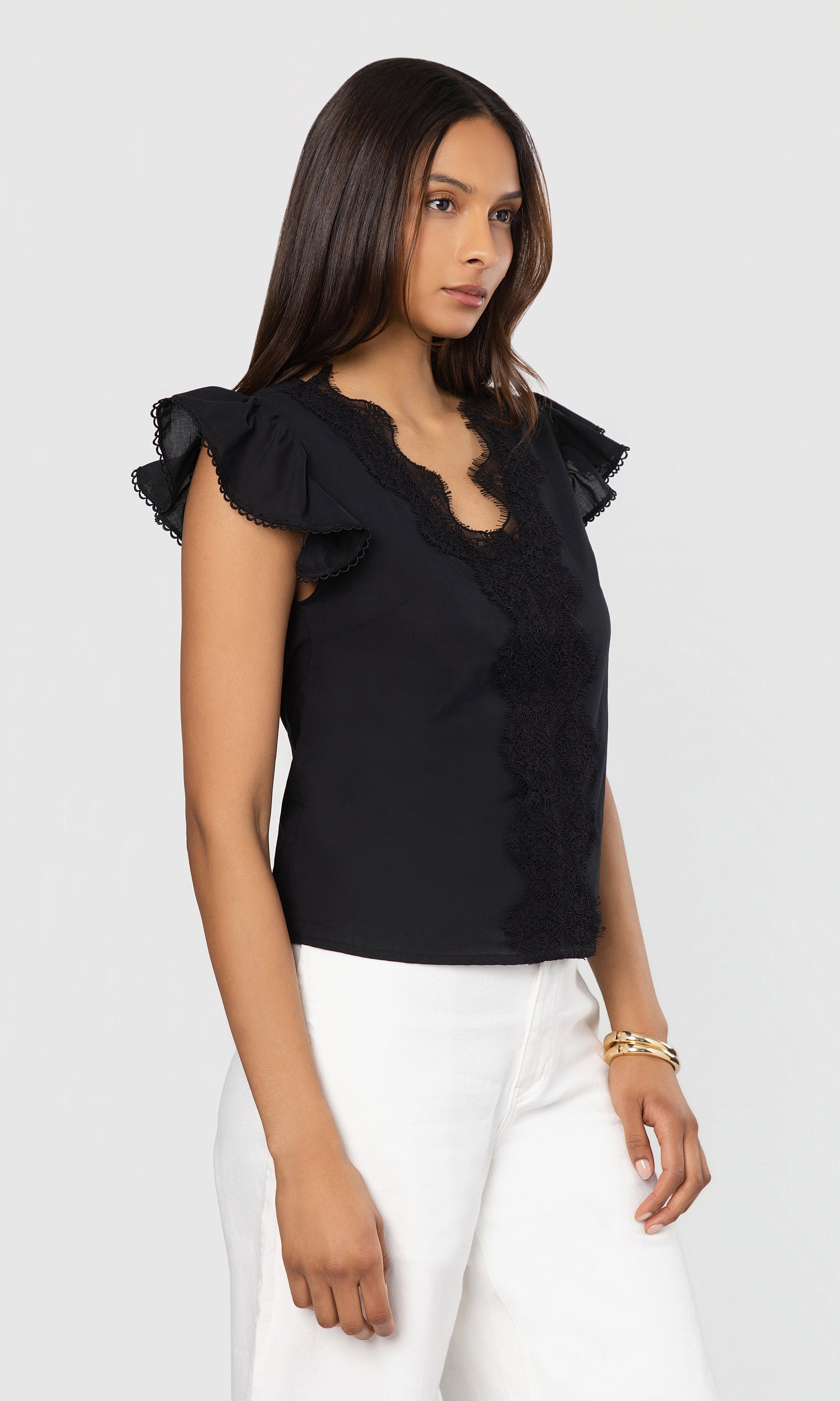 Side view of woman wearing a black top with ruffled sleeves on a white background