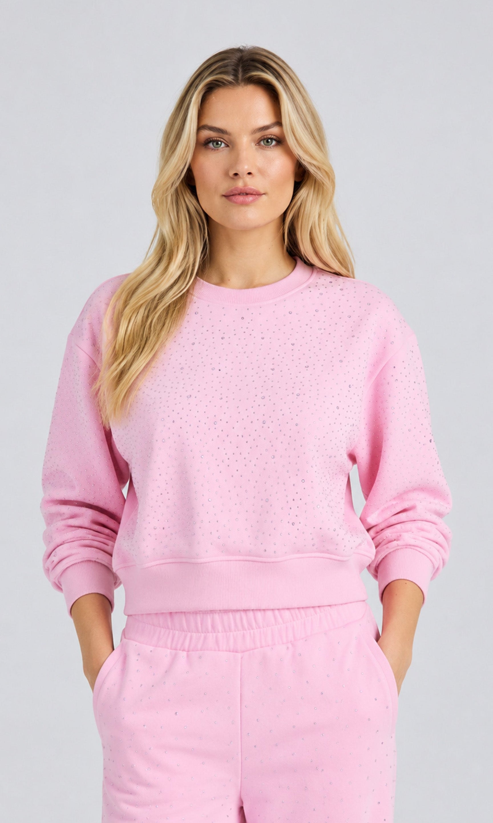 Model wearing a poppy pink sweatshirt with crystal embellishments and matchings pants on a plain background.