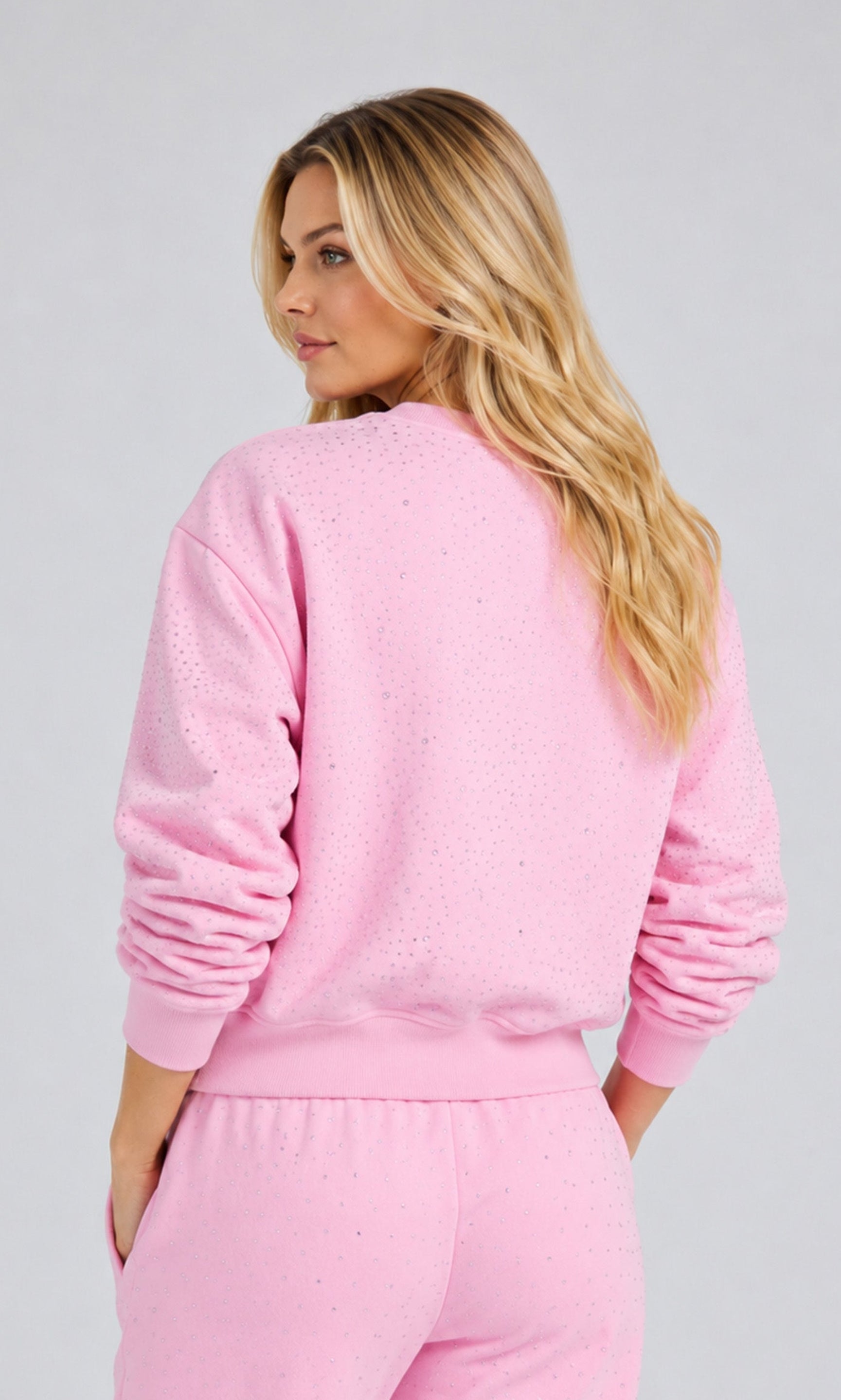 Back view of model wearing a poppy pink sweatshirt with crystal embellishments and matchings pants on a plain background.